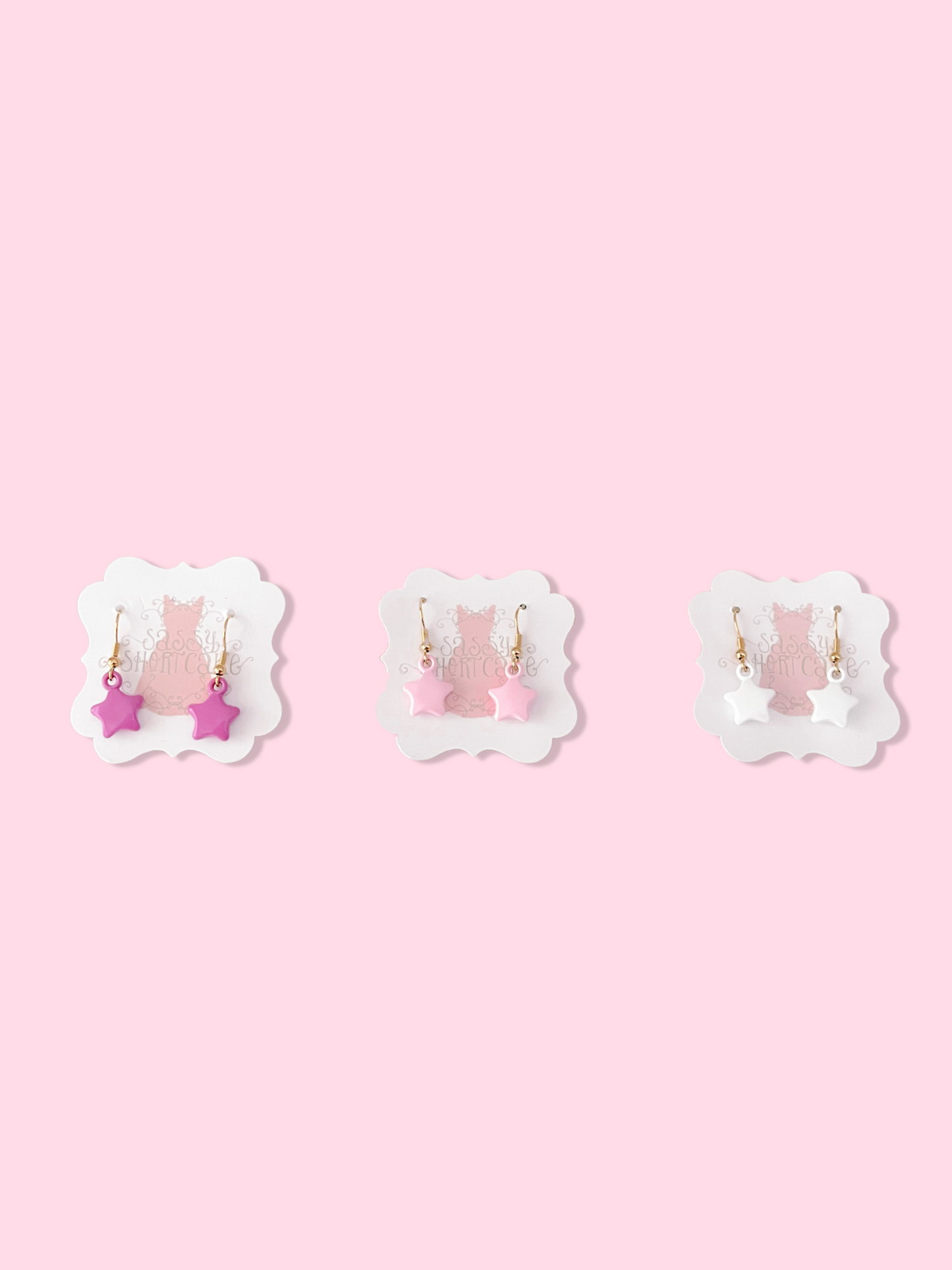Pink, white, and fuchsia star-shaped earrings displayed on pink background.