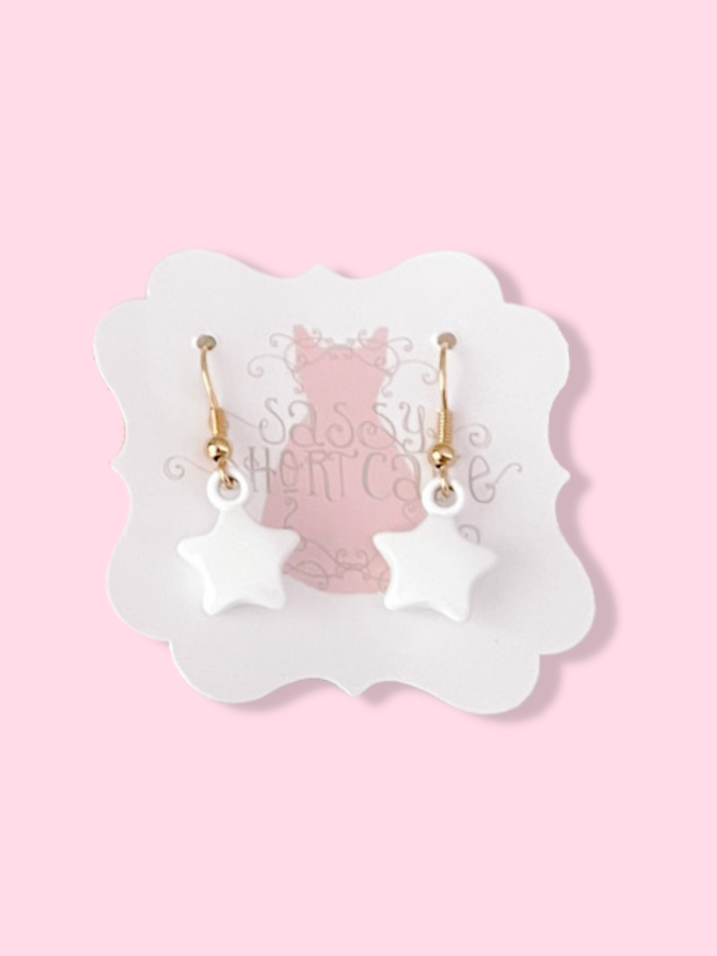 White star-shaped earrings with gold hooks, displayed on a pink background.