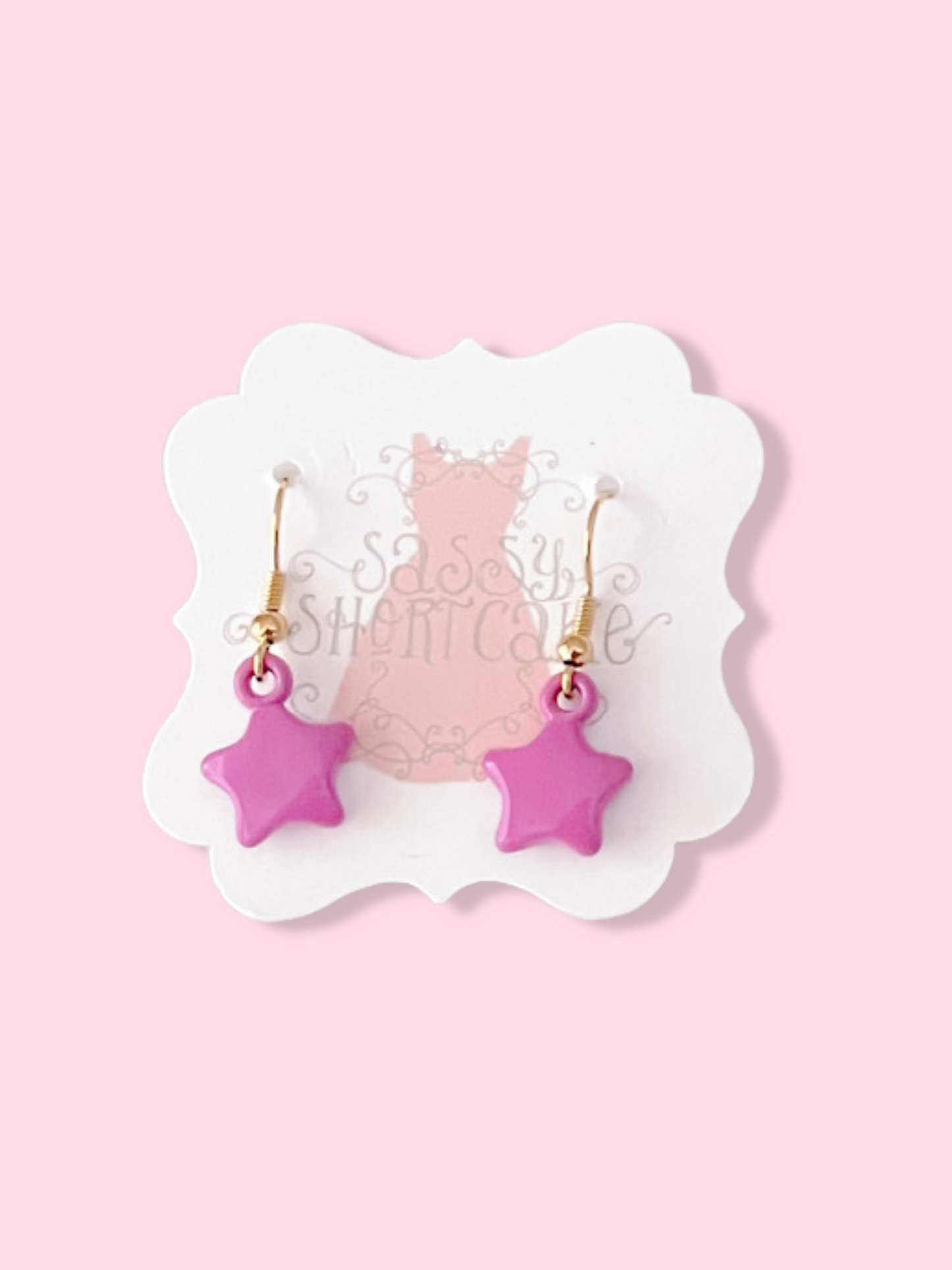 Pink star-shaped earrings on a display card against a pink background.