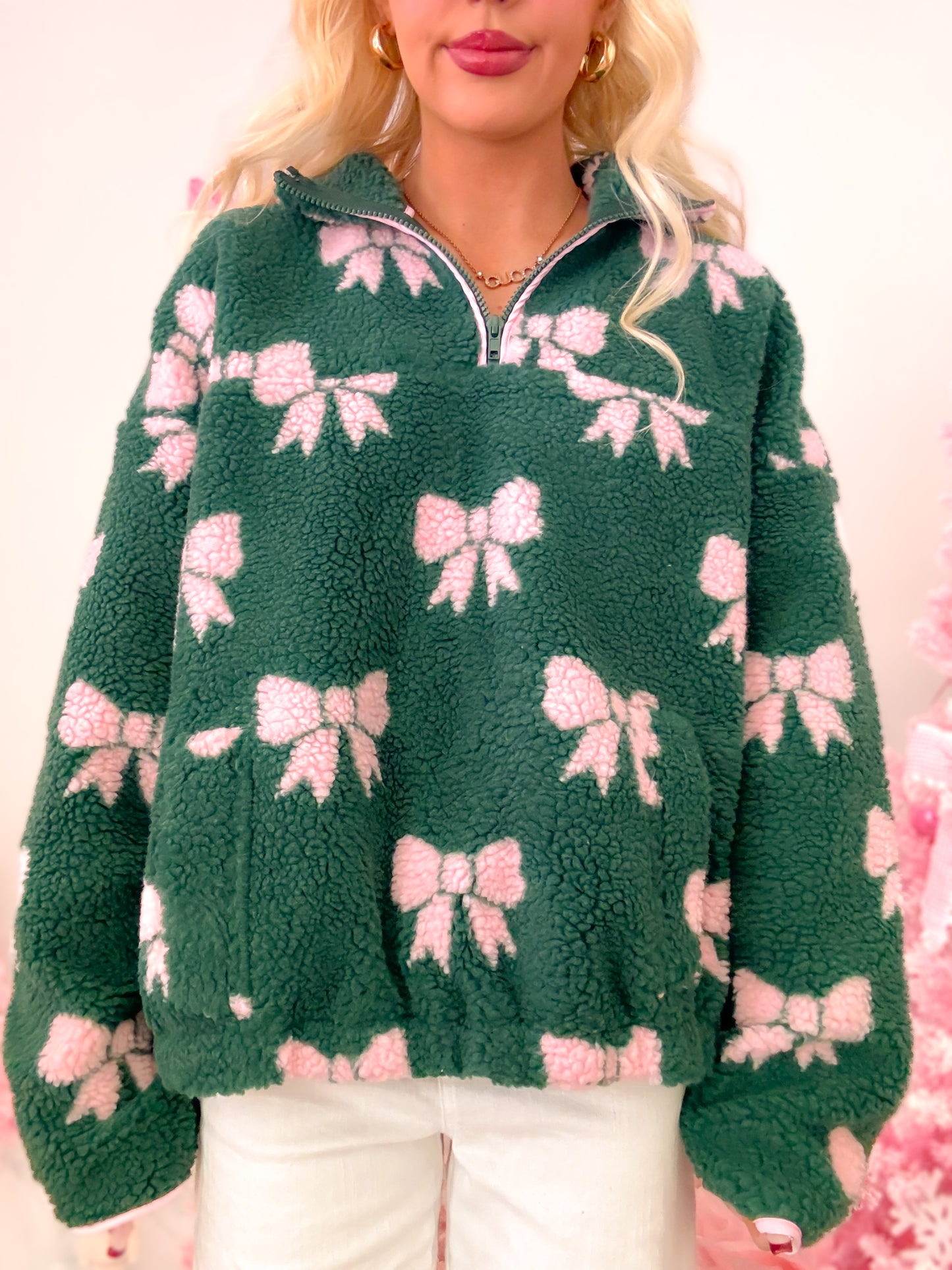 Close-up of the hunter green sherpa pullover, highlighting the soft texture, pink bows, and quarter zip detail.