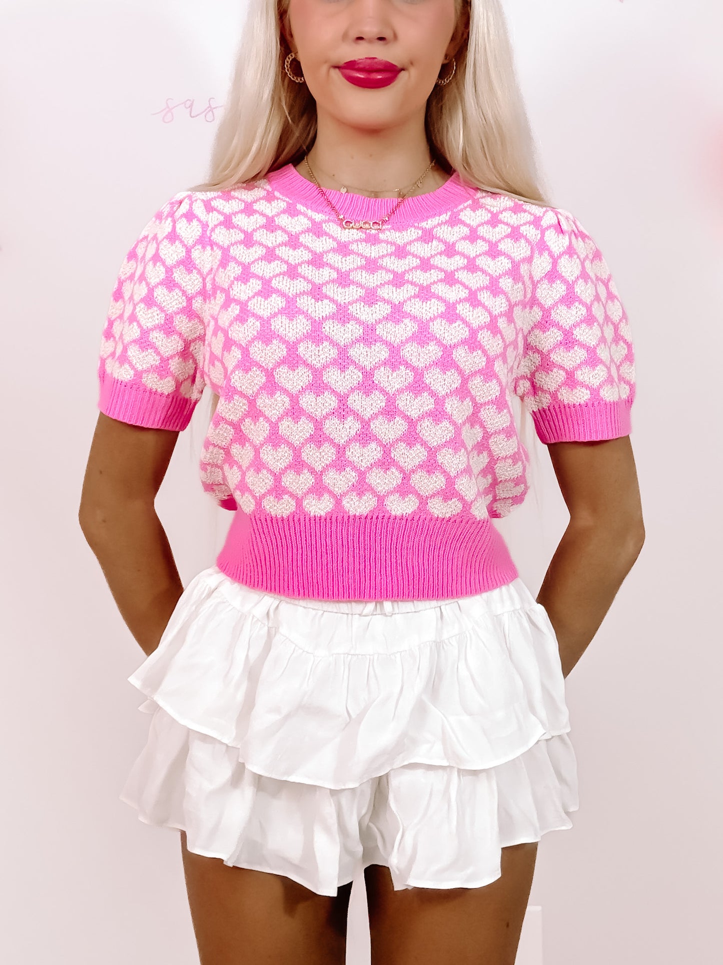 Pink short-sleeve knit top with white heart pattern, modeled with white ruffle shorts.