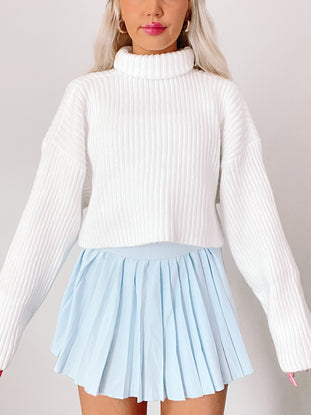 White ribbed knit turtleneck sweater styled with a light blue pleated mini skirt.