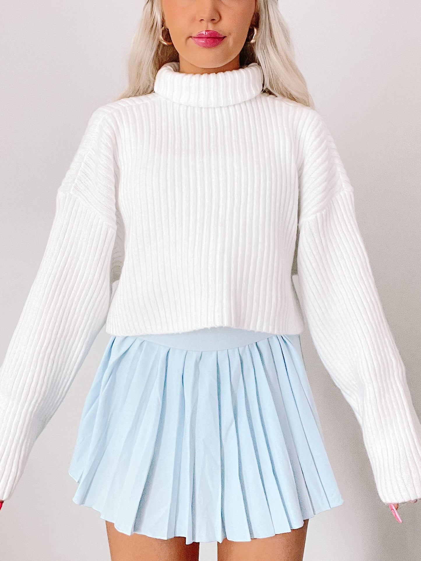 White ribbed knit turtleneck sweater styled with a light blue pleated mini skirt.