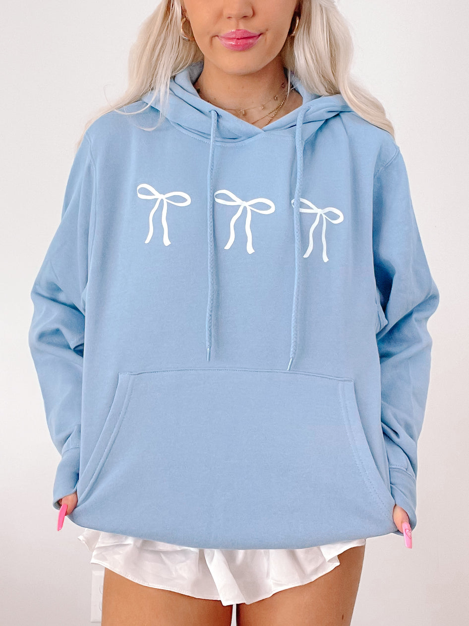 Light blue hoodie featuring three white bows, casual style.