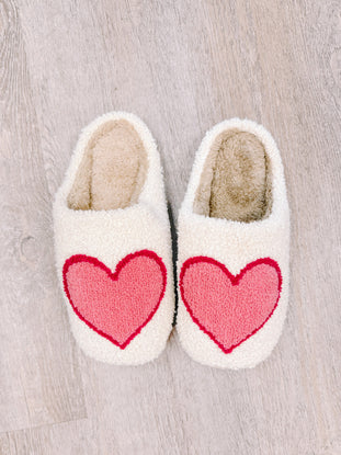 Cozy cream slippers with pink heart detail for relaxing at home.