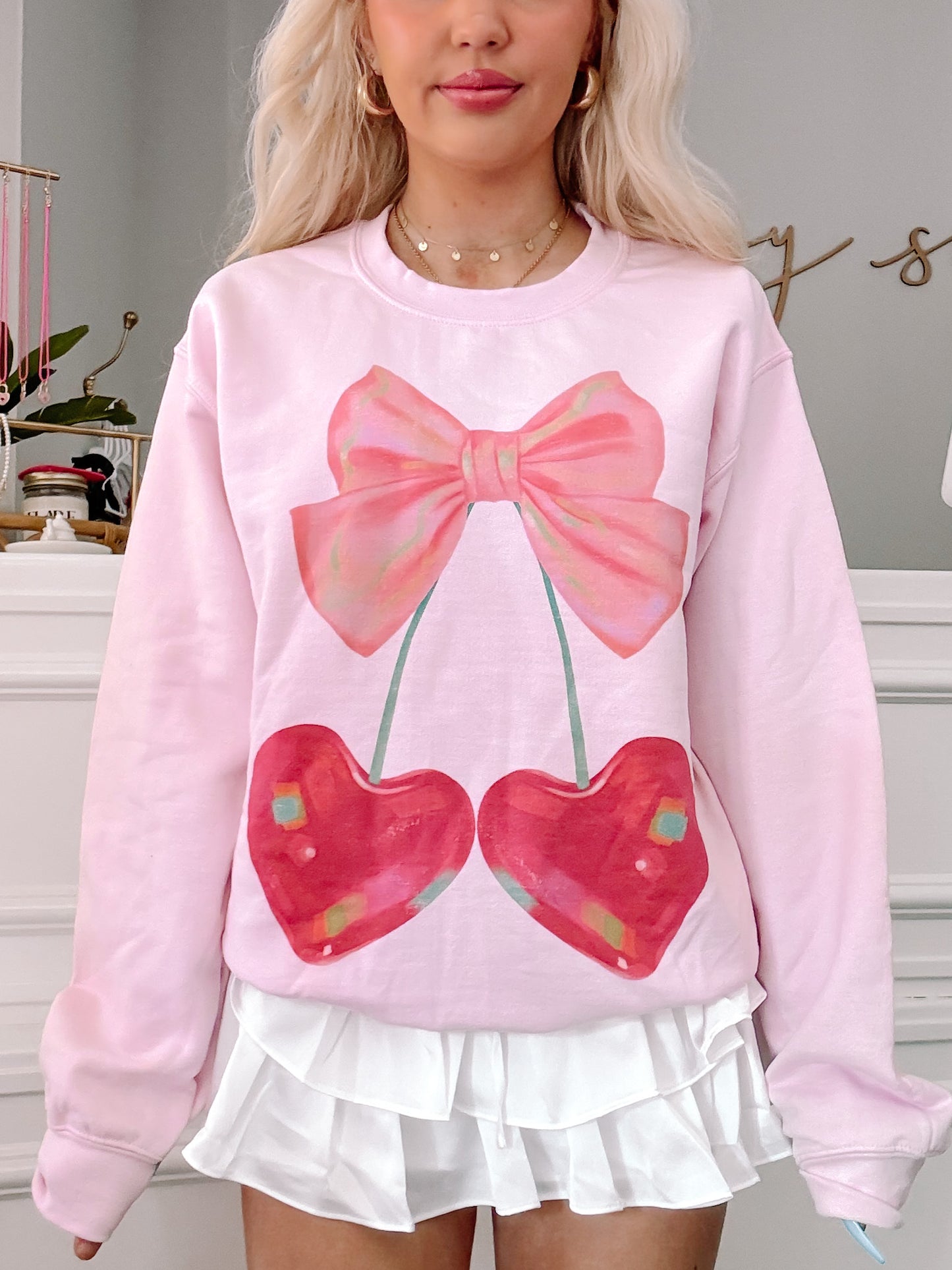 Pink crewneck sweatshirt featuring a whimsical illustration of cherries and a bow.