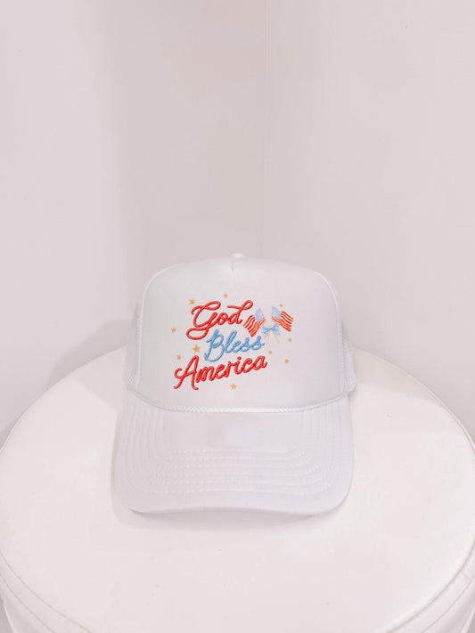 White trucker hat with "God Bless America" embroidered in red and blue, featuring small American flag from sassy shortcake