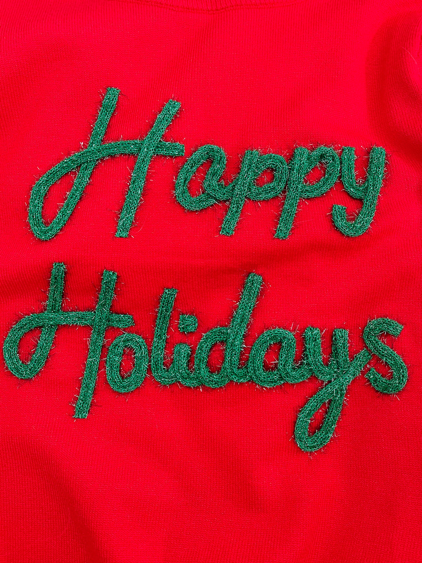 Red knit sweater detail featuring green embroidered "Happy Holidays" lettering.