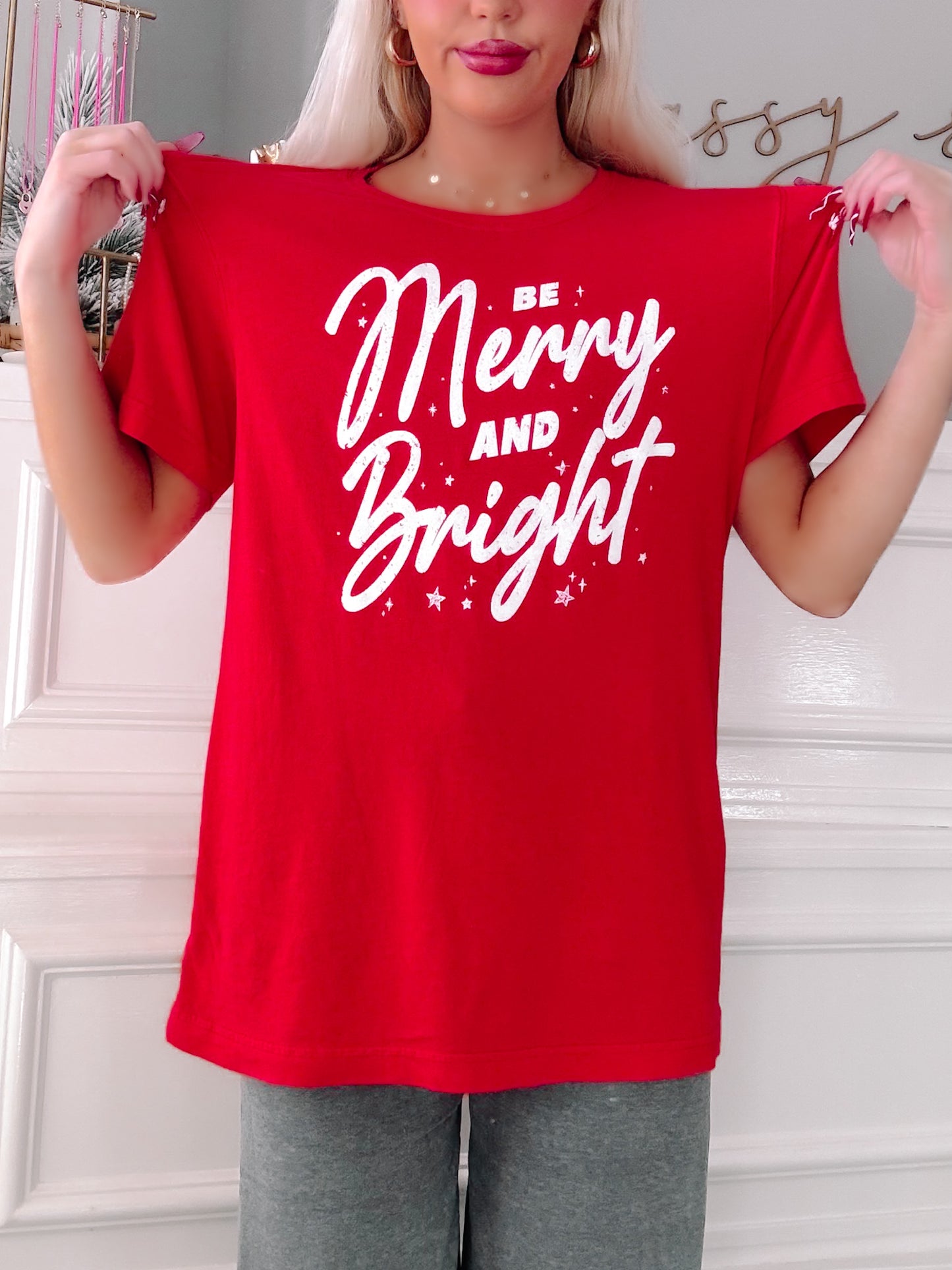 Person wearing a red t-shirt with 'Be Merry and Bright' text.