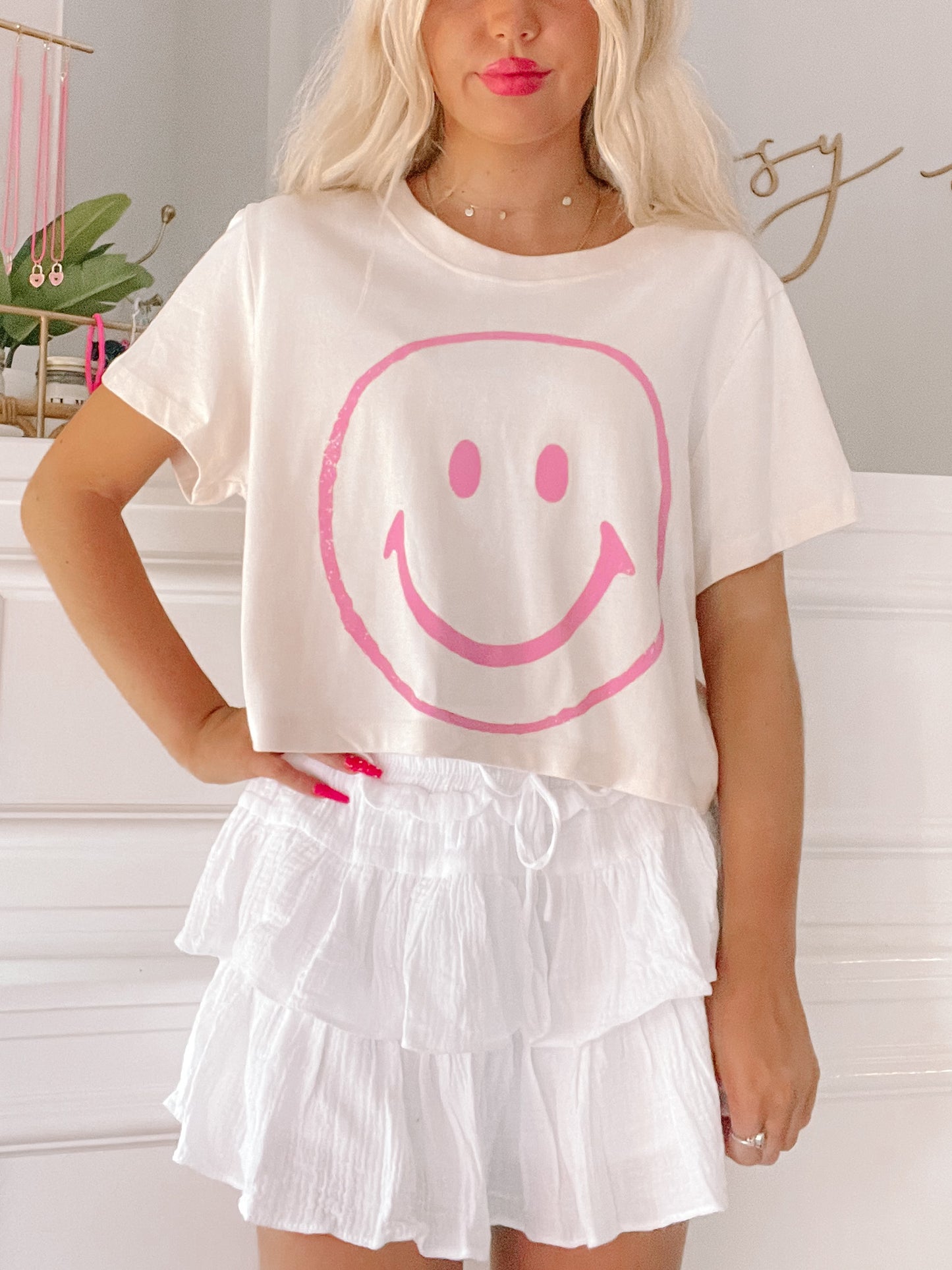 Cream cropped tee featuring a pink smiley face graphic, styled with a white tiered skirt.