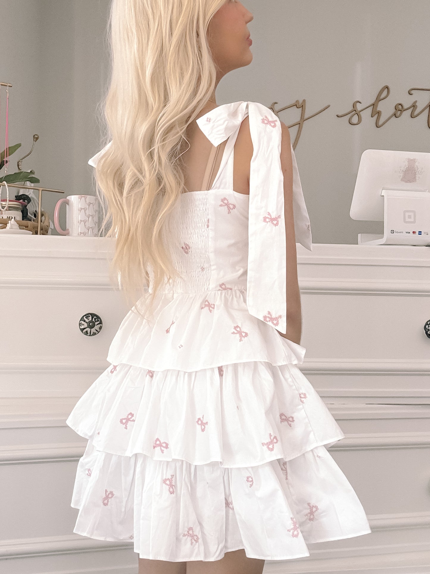 White tiered mini dress with pink embroidered bows, shown from the back.