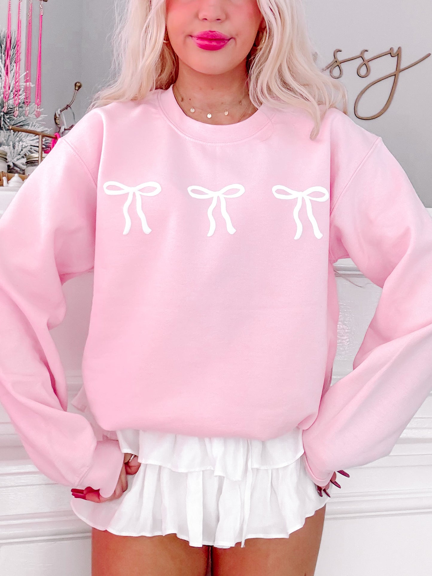 Pink crewneck sweatshirt with three white bows, styled with a white ruffle skirt.