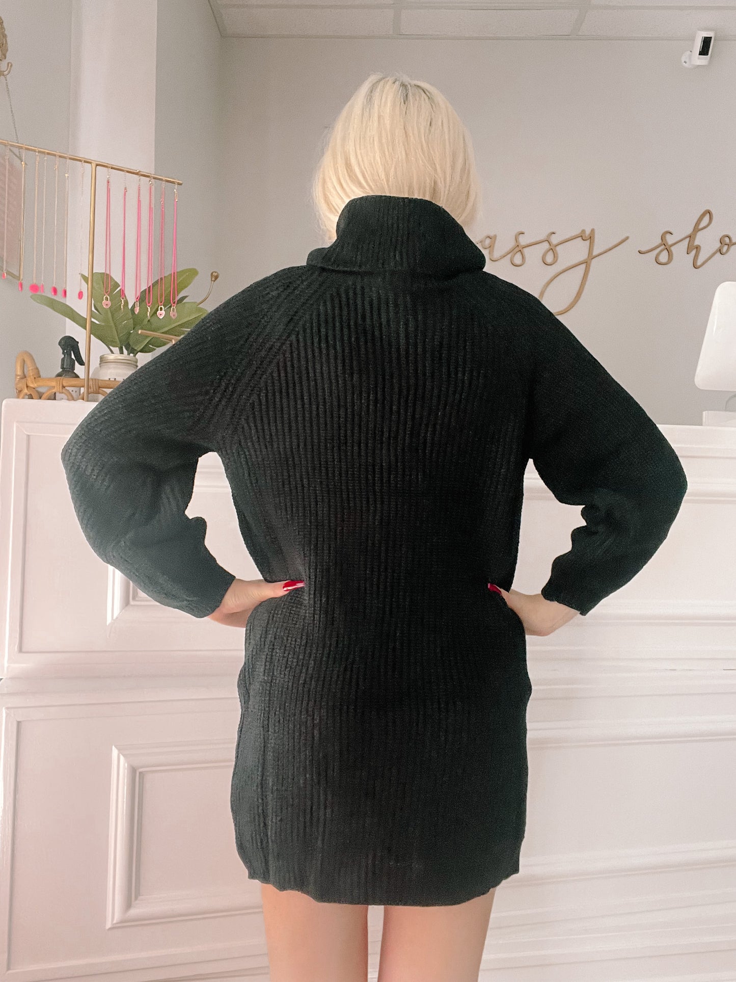 Black ribbed knit turtleneck sweater dress, seen from behind in a shop.