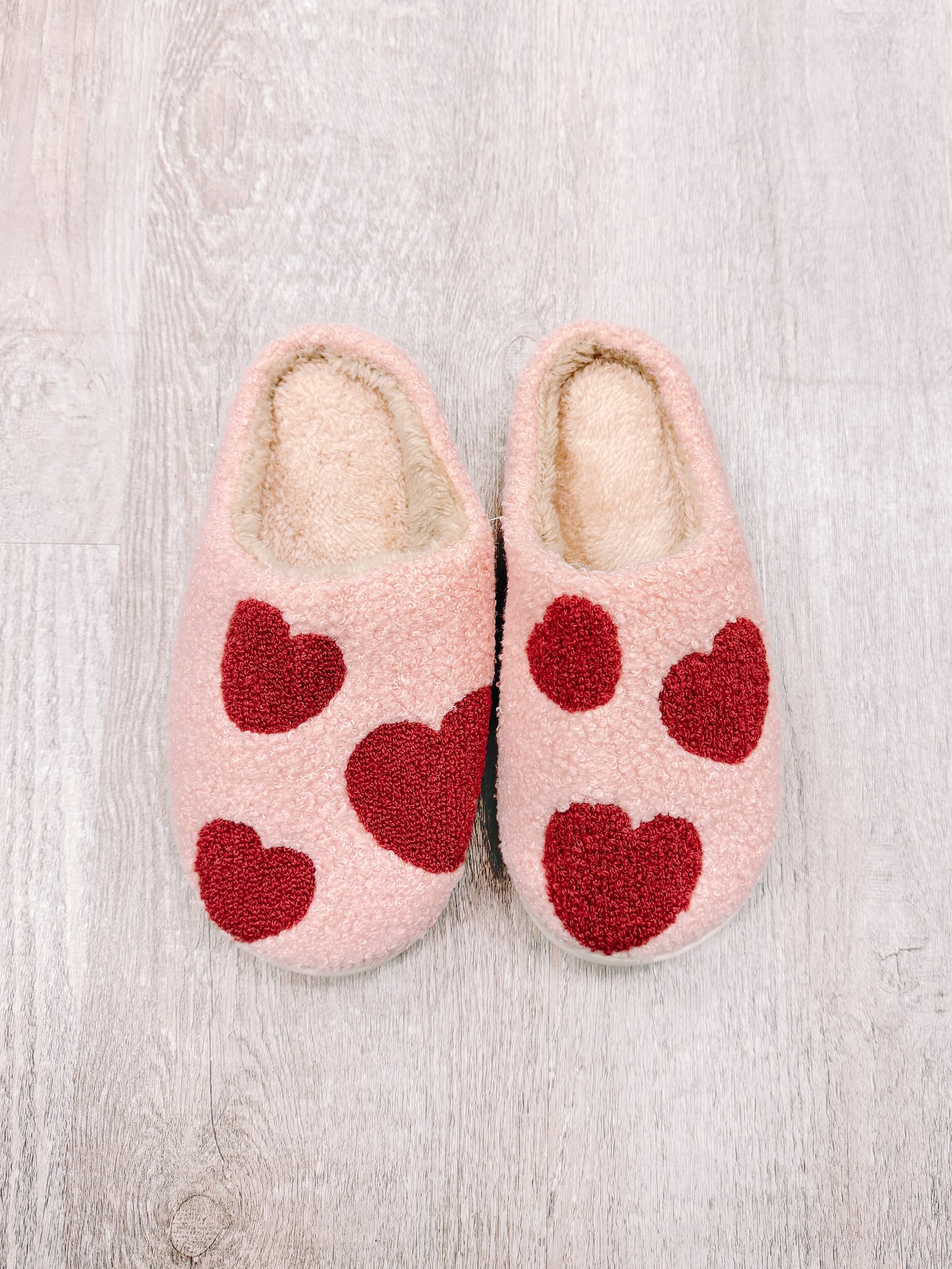 Pink fuzzy slippers with red heart accents for cozy comfort.