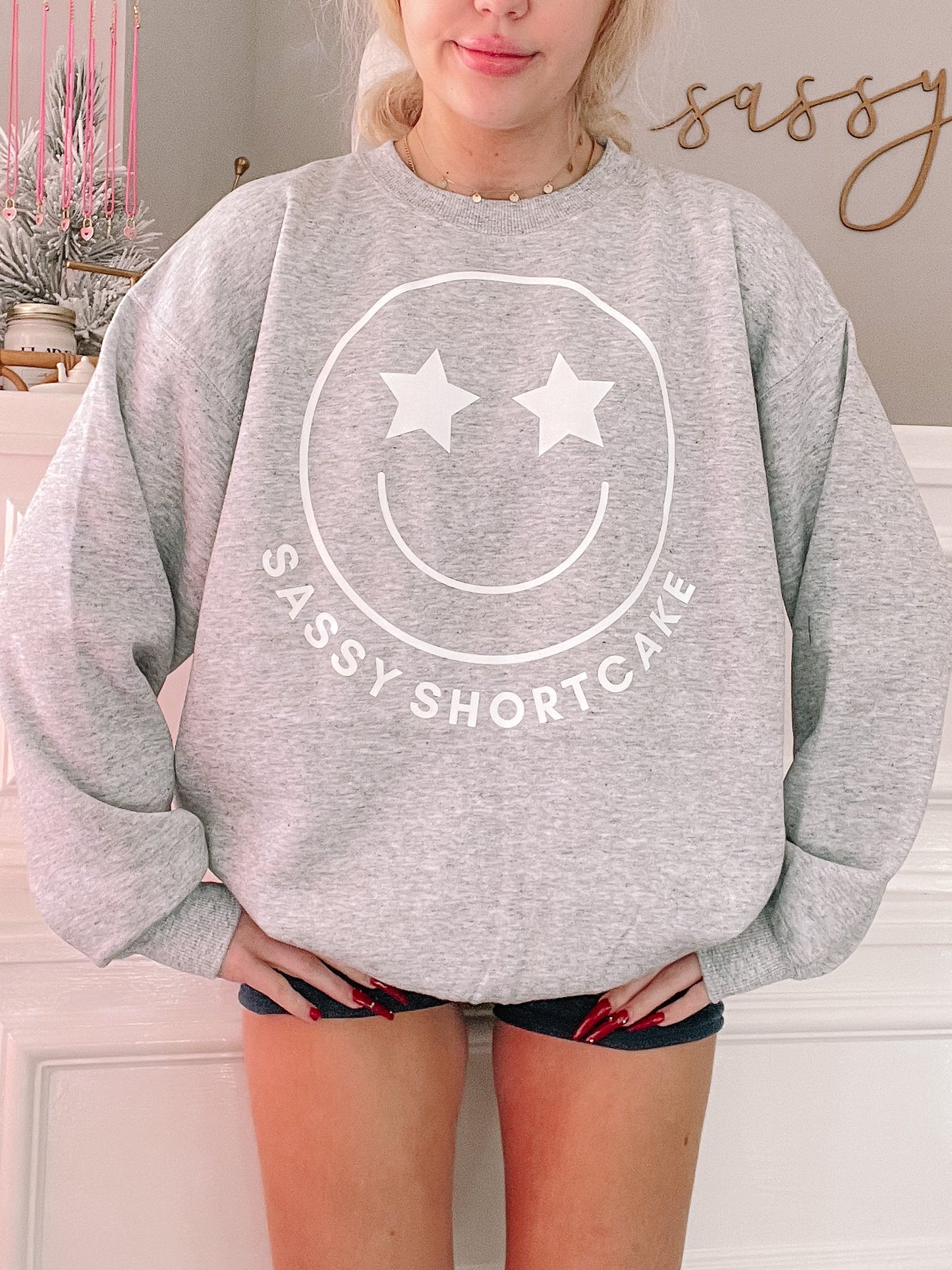 Grey Sassy Shortcake Smiley Crewneck sweatshirt with star-eye smiley face graphic. Sassy Merch