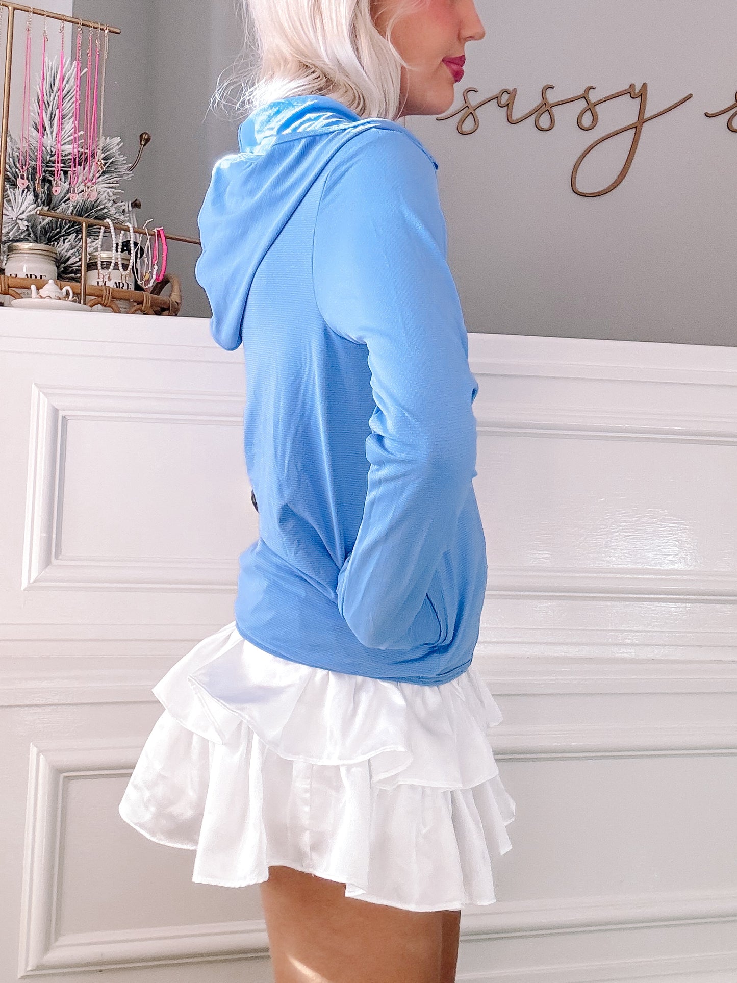 Light blue zip-up jacket with a white ruffled skirt, shown against a white wall.