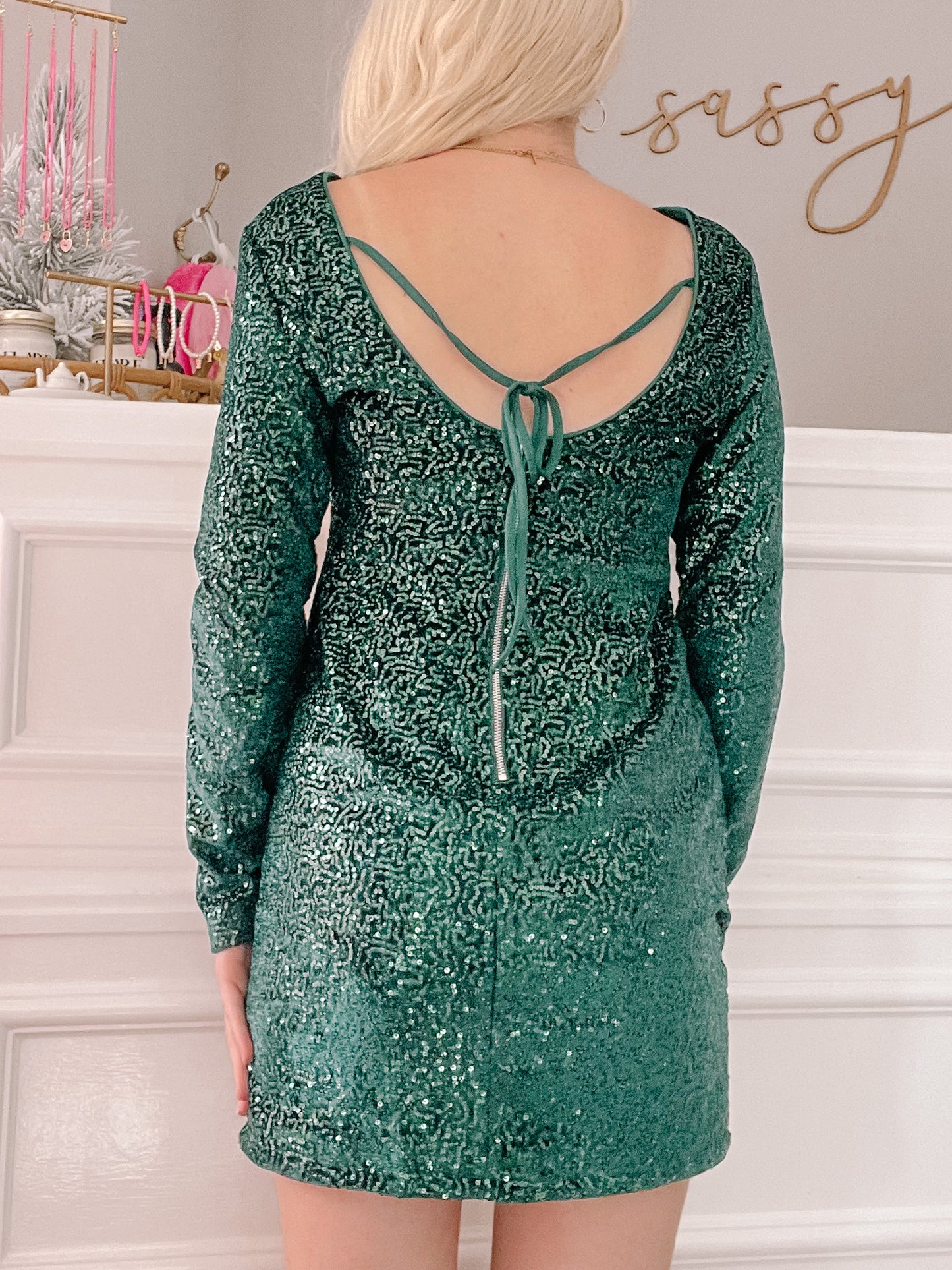 Dark green sequin mini dress with long sleeves and a low back; tie detail.