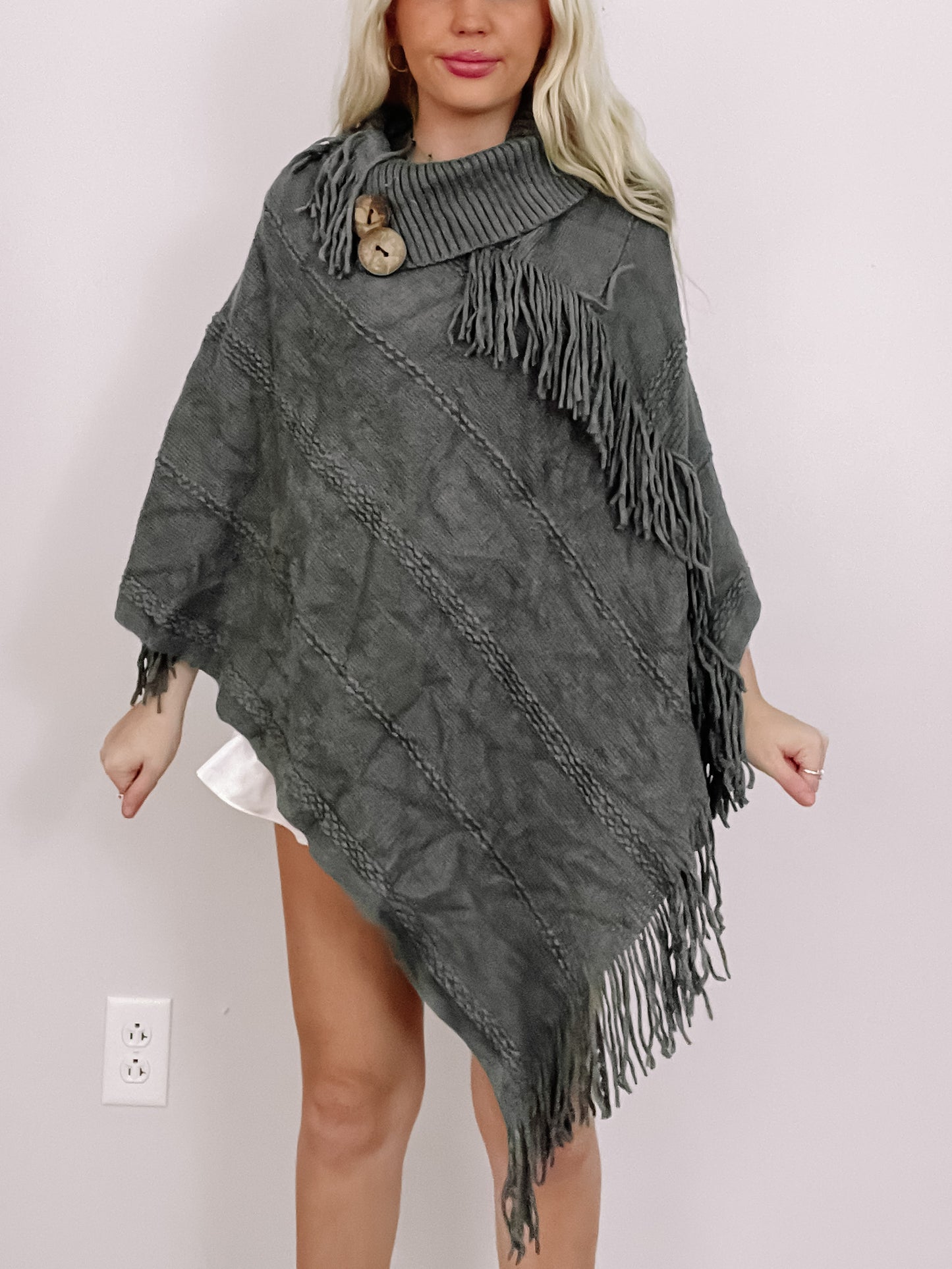 Gray knit poncho with fringe detail and wooden buttons.