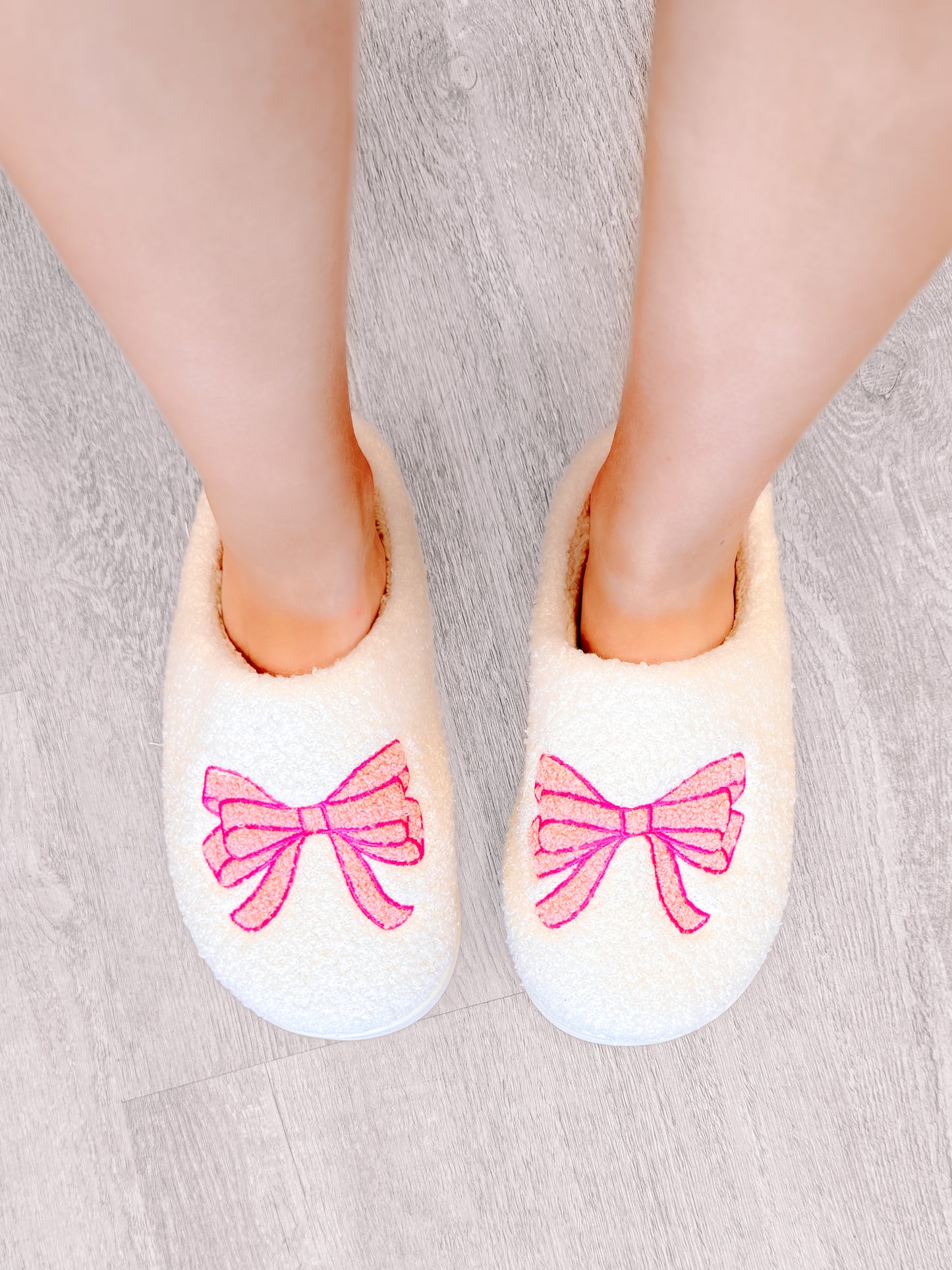 White fuzzy slippers with pink bows, cozy and comfortable footwear.