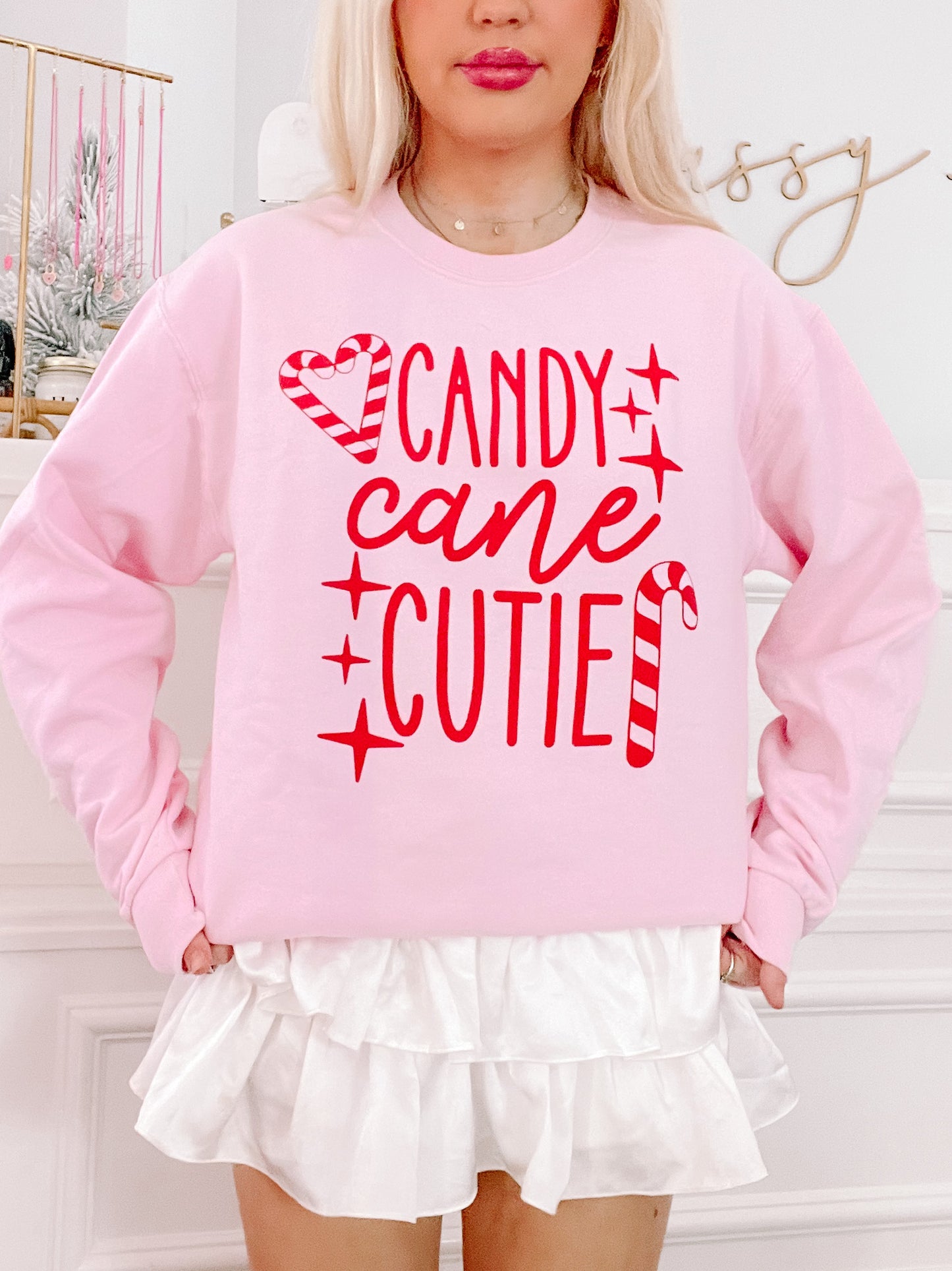Pink crewneck sweatshirt with red candy cane design and festive text.