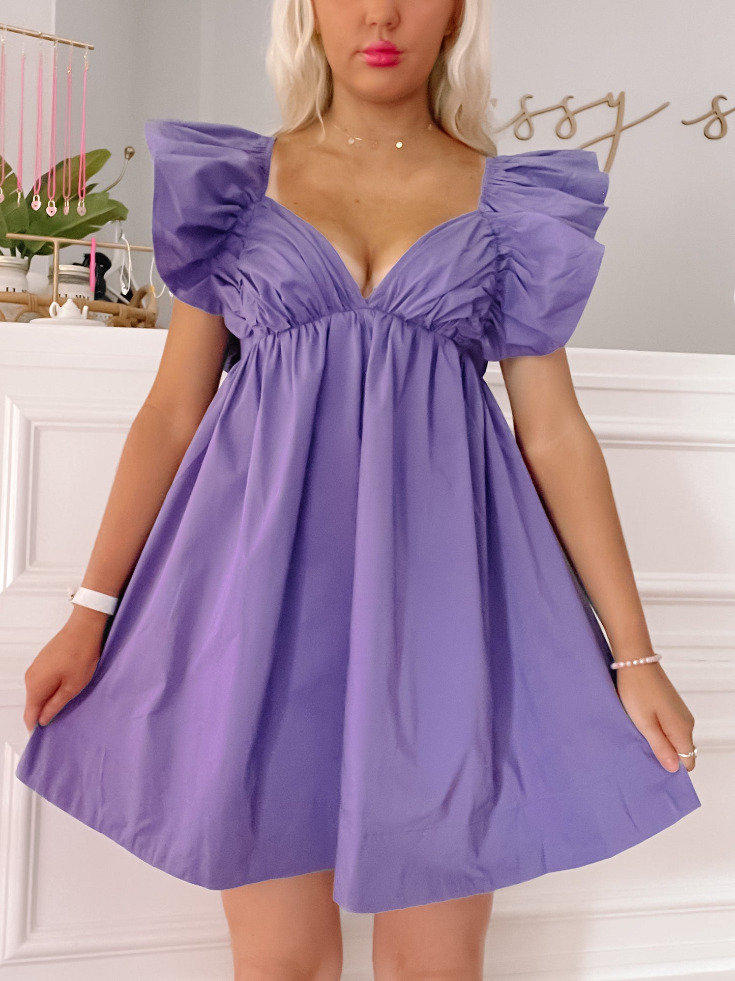 Purple mini dress with ruffled sleeves; a woman models it in a bright room.