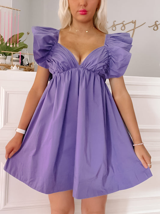 Purple mini dress with ruffled sleeves; a woman models it in a bright room.