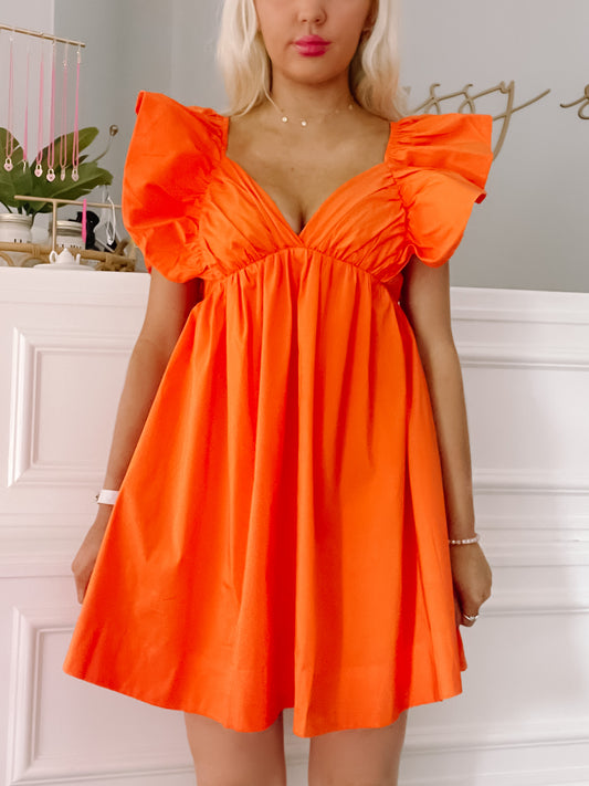 Bright orange mini dress with ruffled sleeves, shown on a model against a white wall.