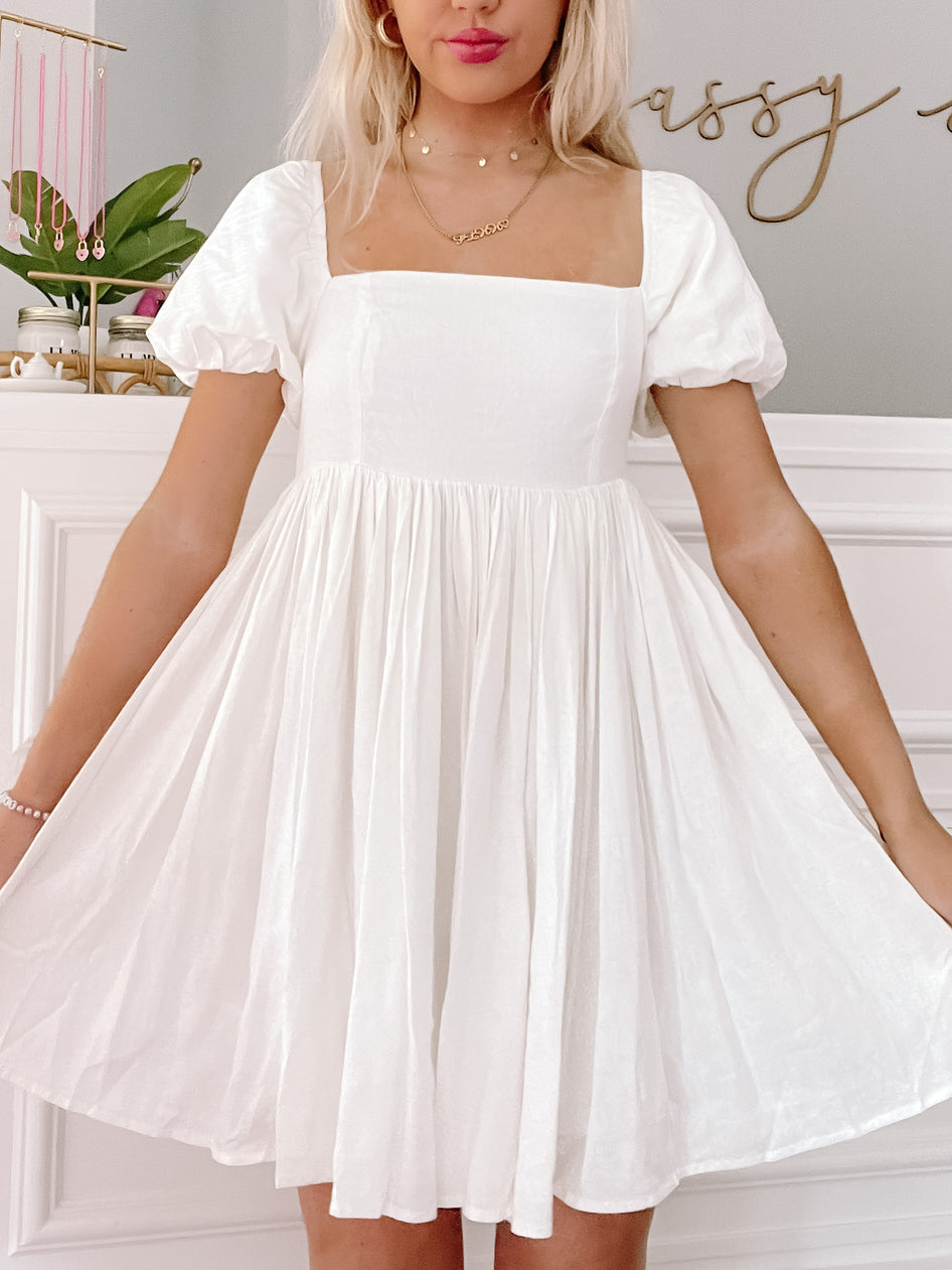 Ivory mini dress with puff sleeves and a square neckline, shown on a model in a home setting.