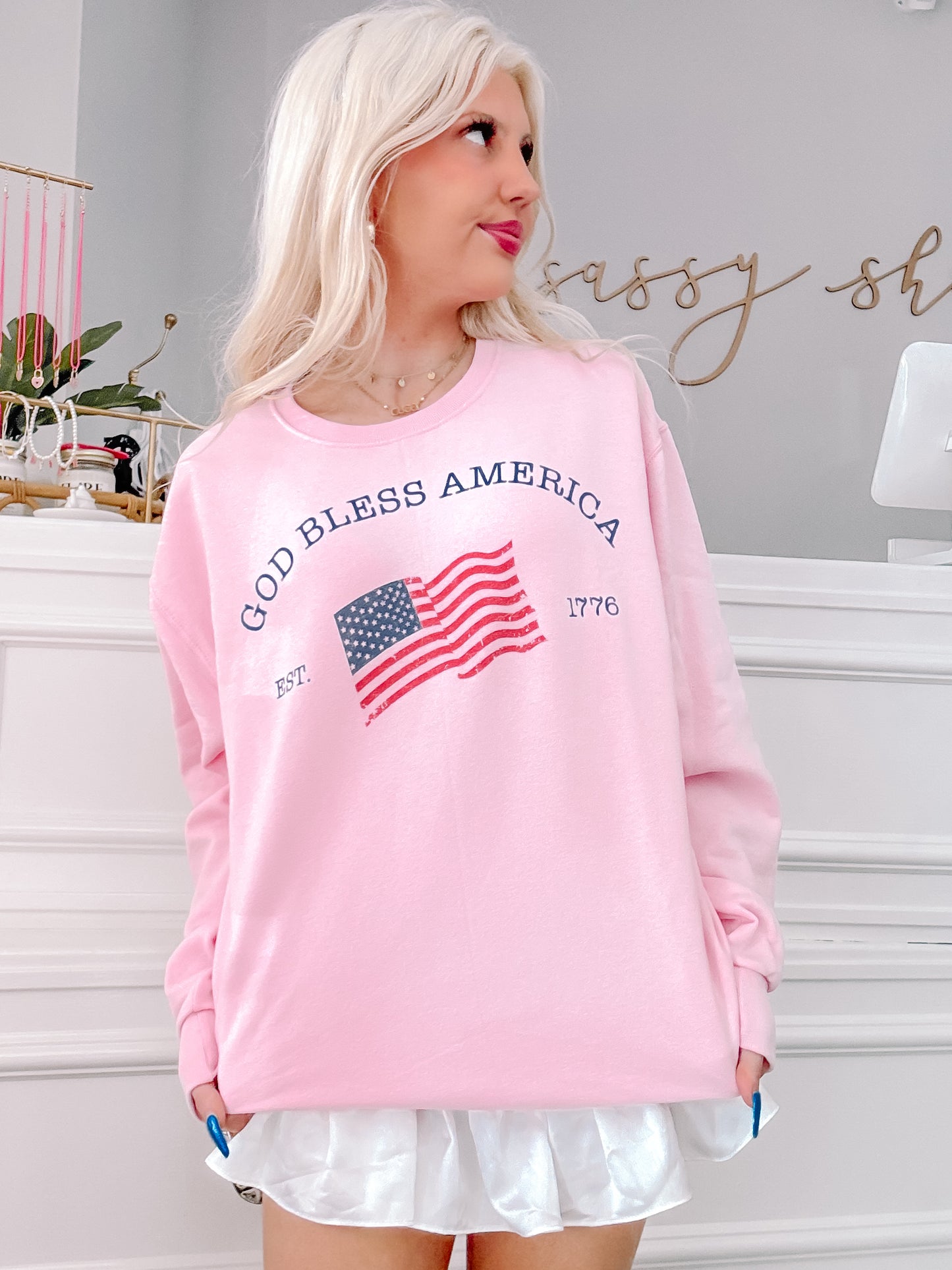 Pink crewneck sweatshirt featuring an American flag graphic and "God Bless America" text.