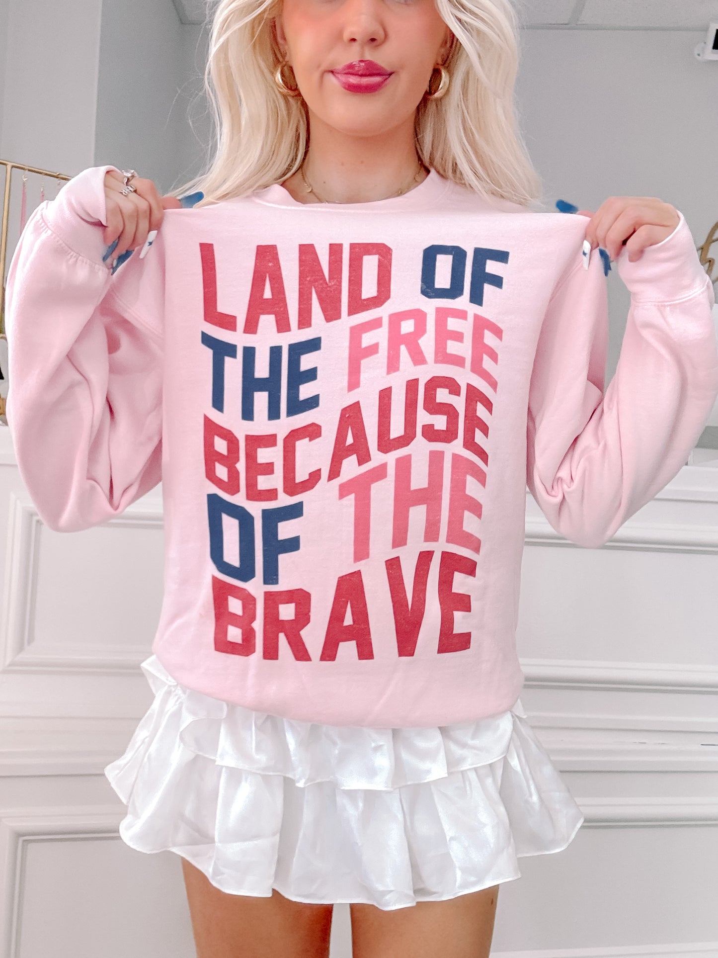 Pink crewneck sweatshirt with patriotic text graphic; woman modeling.