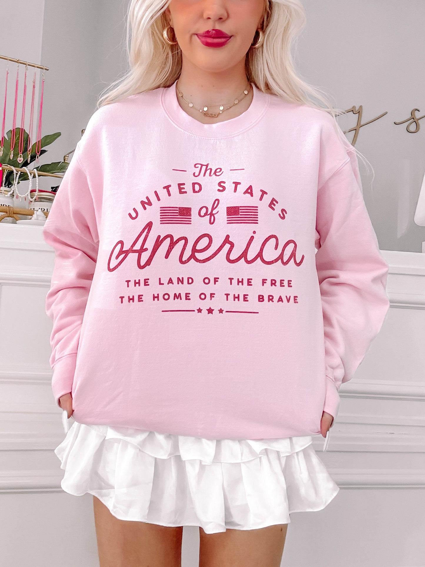 Pink crewneck sweatshirt with patriotic graphic, styled with a white ruffle skirt.