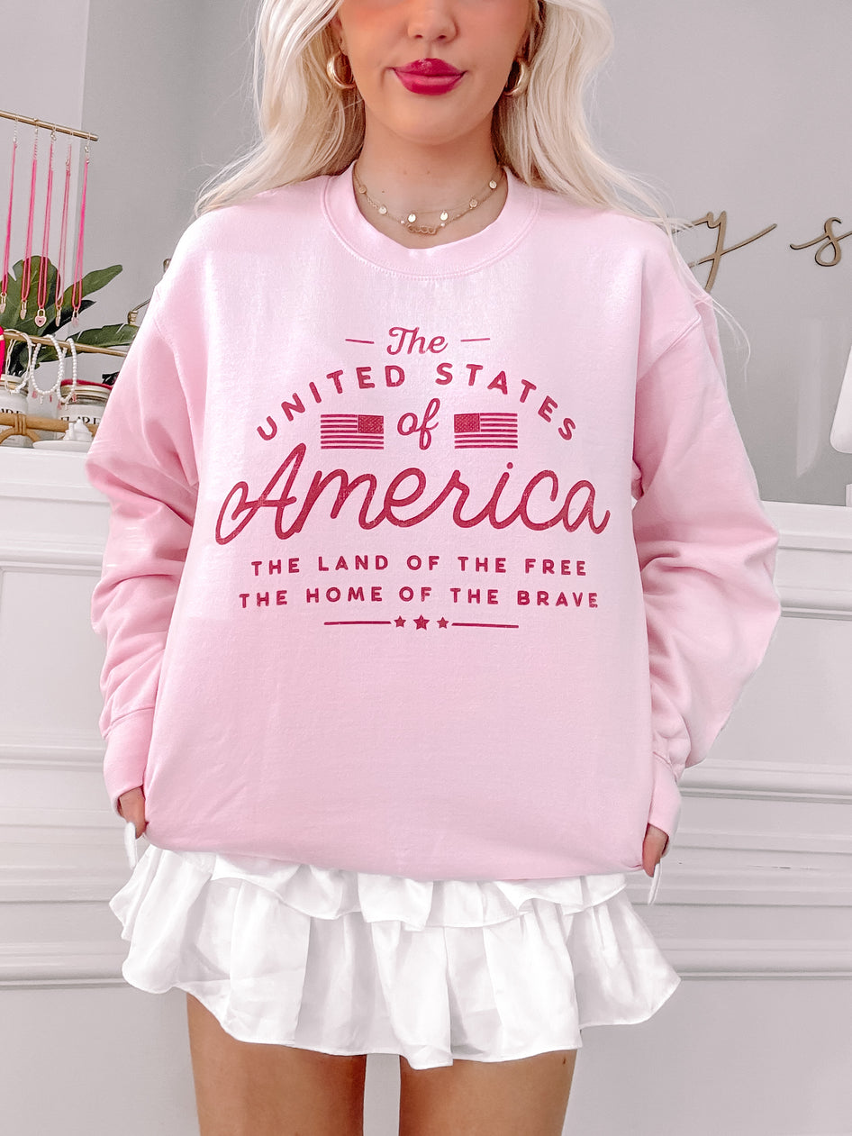 Pink crewneck sweatshirt with patriotic graphic, styled with a white ruffle skirt.