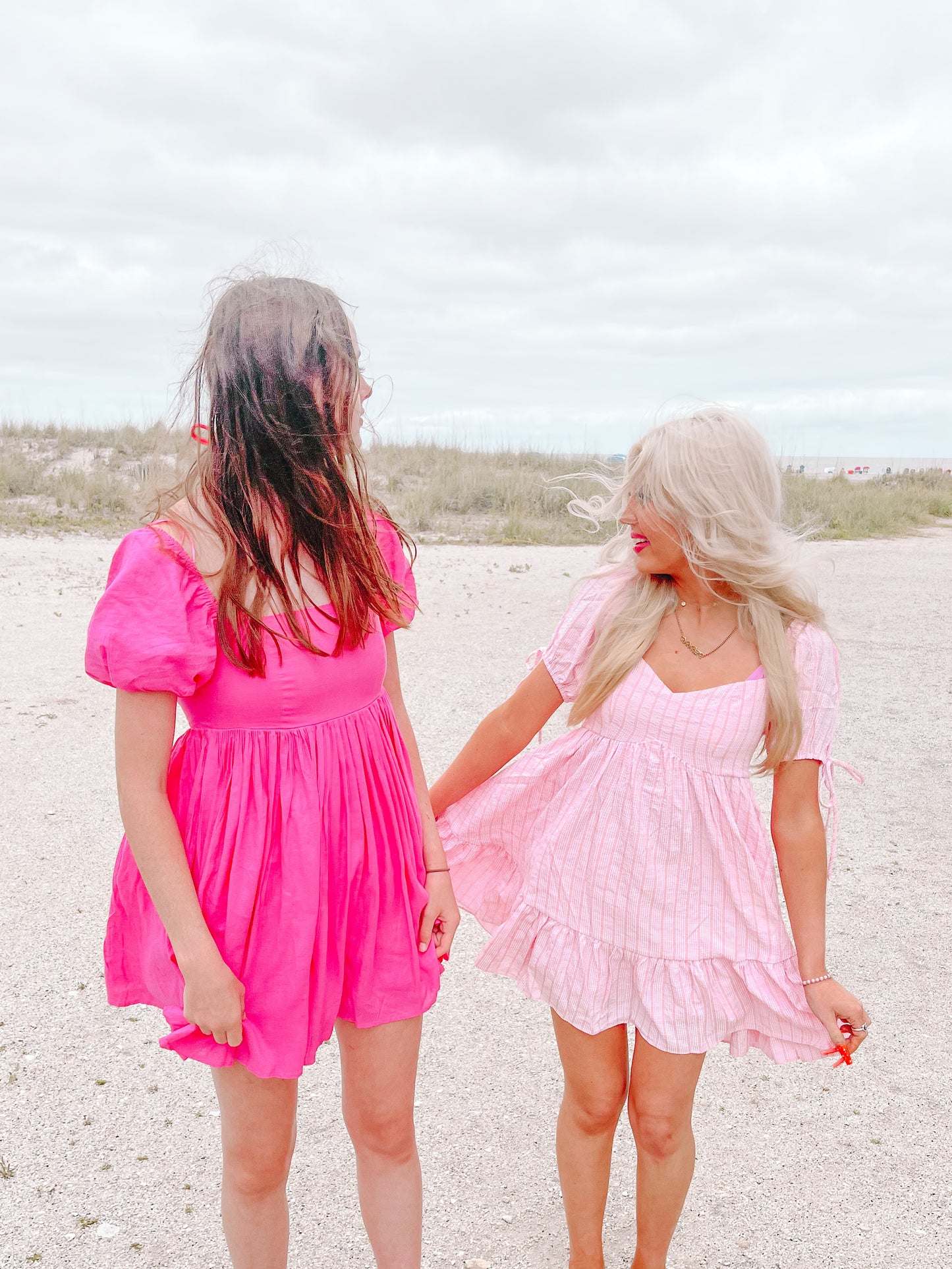 Beach scene with two women wearing pink summer dresses.