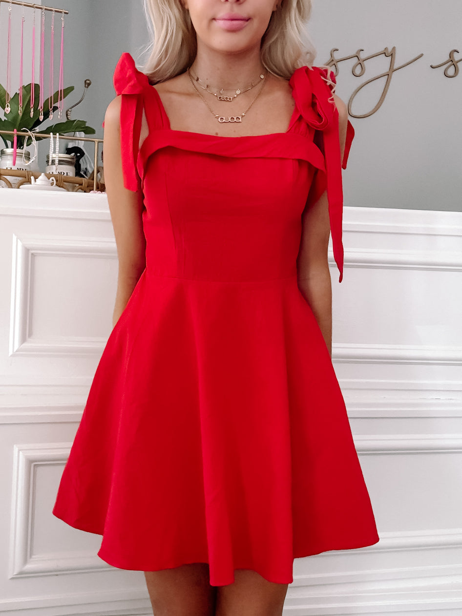 Red fit-and-flare dress with shoulder ties, shown on a model against a white wall.