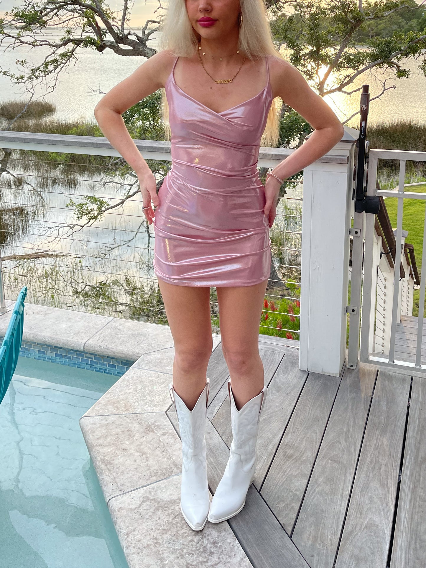Pink metallic mini dress paired with white cowboy boots by a pool at sunset.