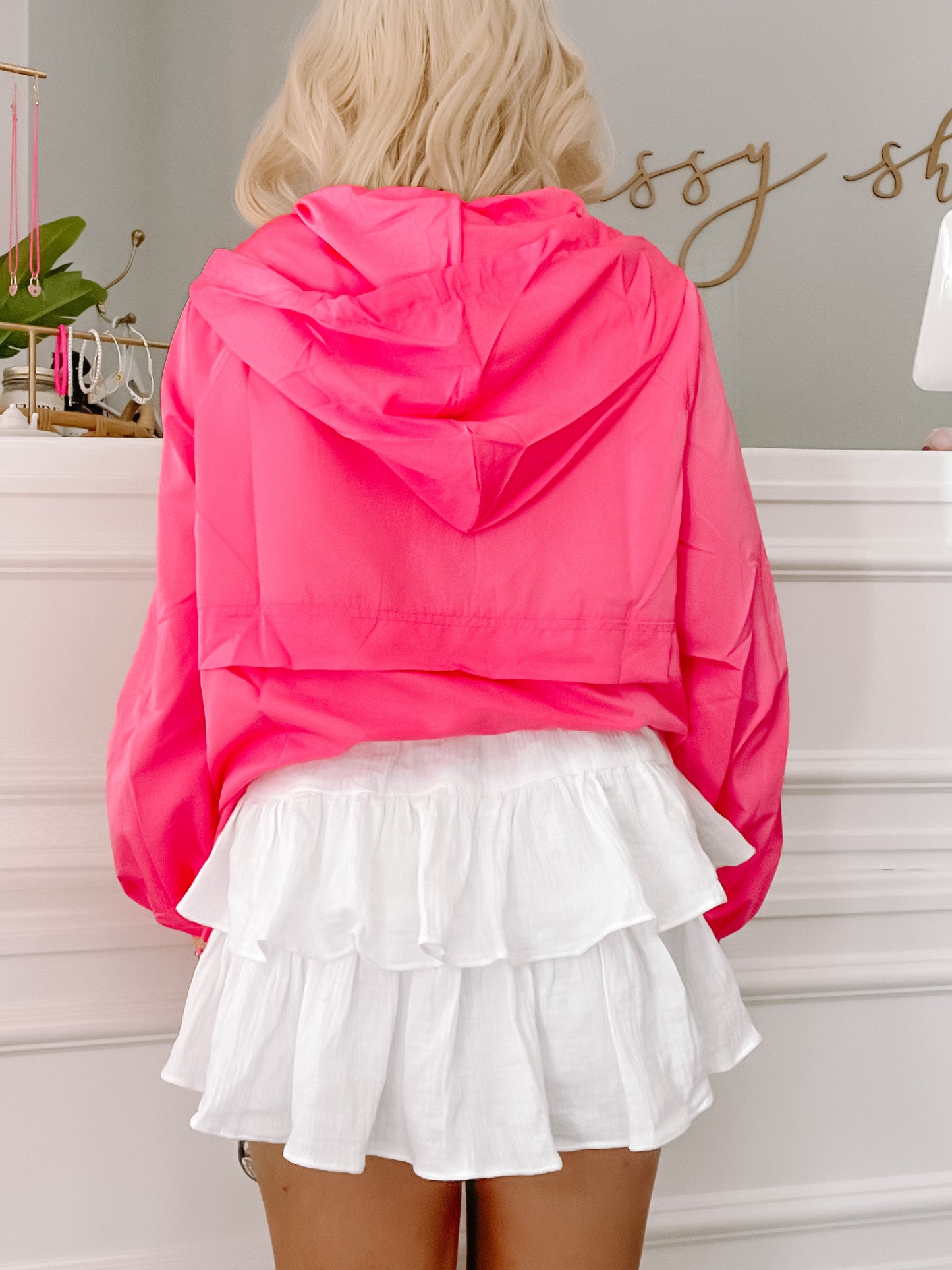 Bright pink hooded jacket paired with a white ruffled mini skirt, shown from the back.