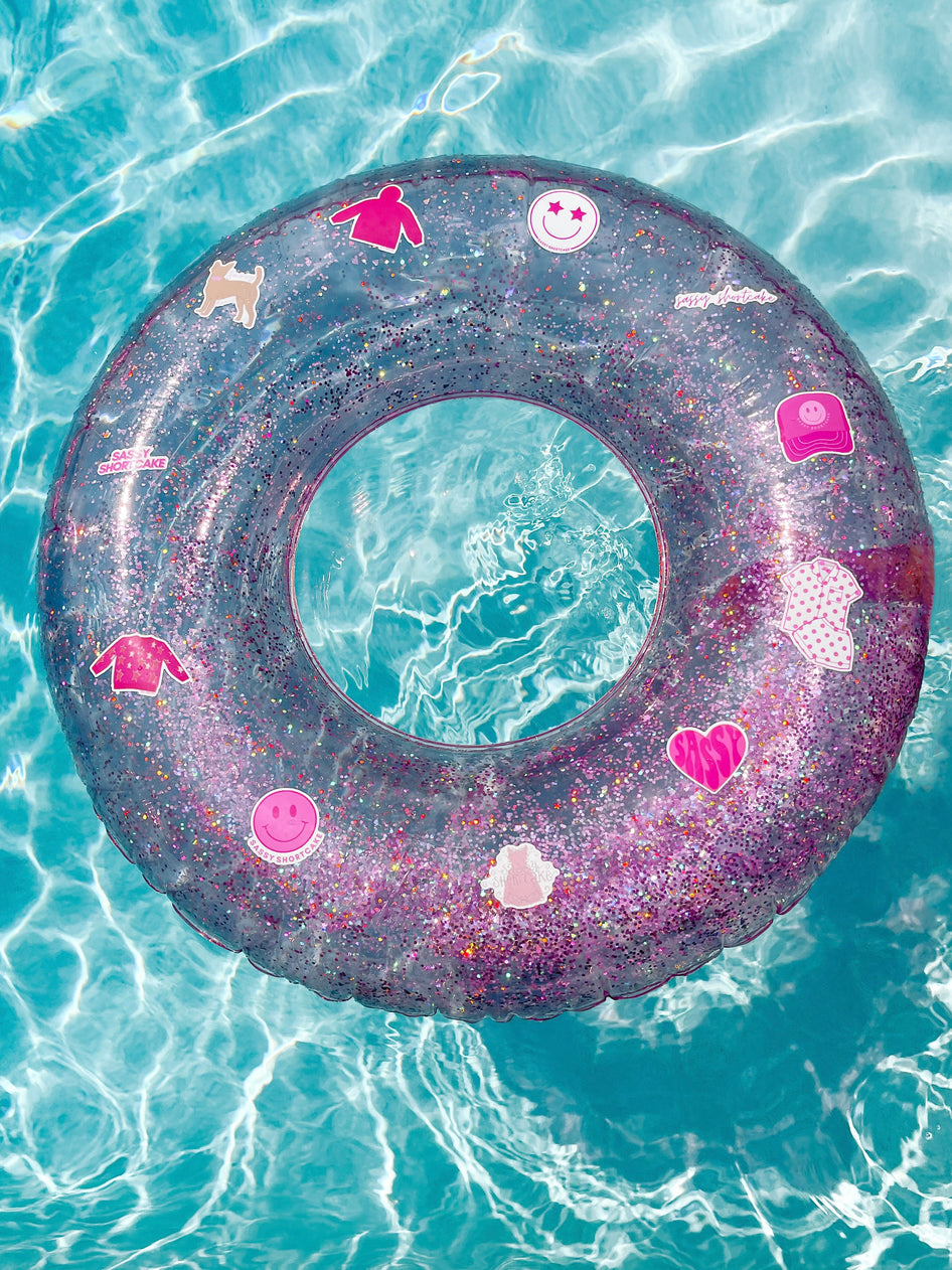 Pink glitter pool float with fun stickers, floating in turquoise water.