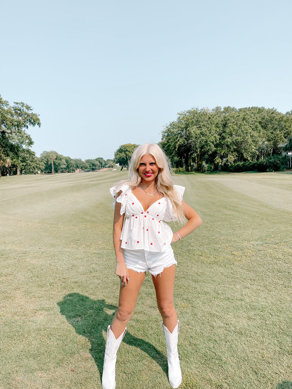 White embroidered star top paired with denim shorts, modeled outdoors on a sunny day.