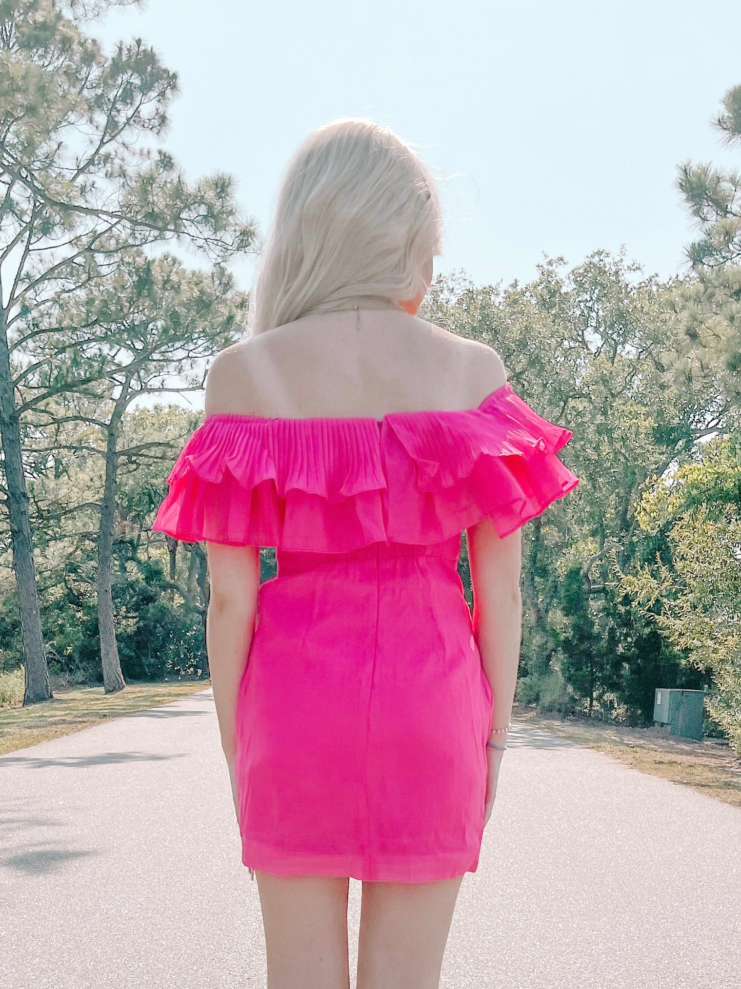 Hot pink mini dress with ruffled off-the-shoulder neckline, shown outdoors.