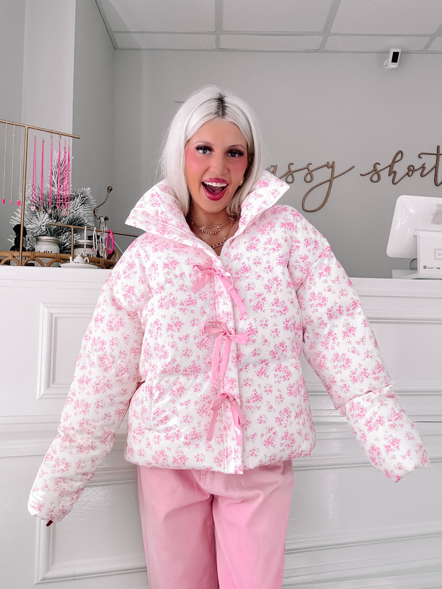 Pink floral puffer jacket with ribbon detailing, modeled in a boutique setting.