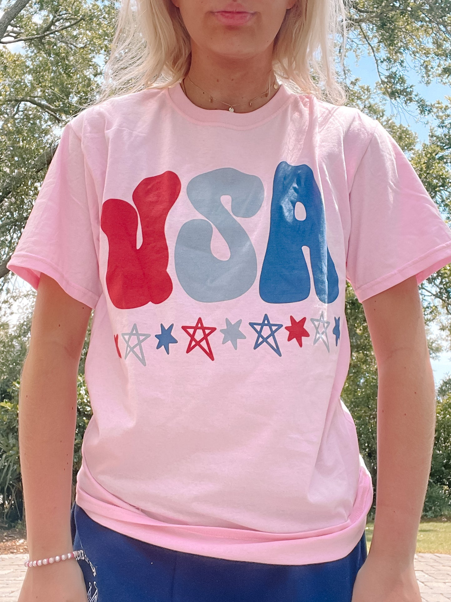 Light pink t-shirt featuring a retro-style USA graphic with stars, modeled outdoors.