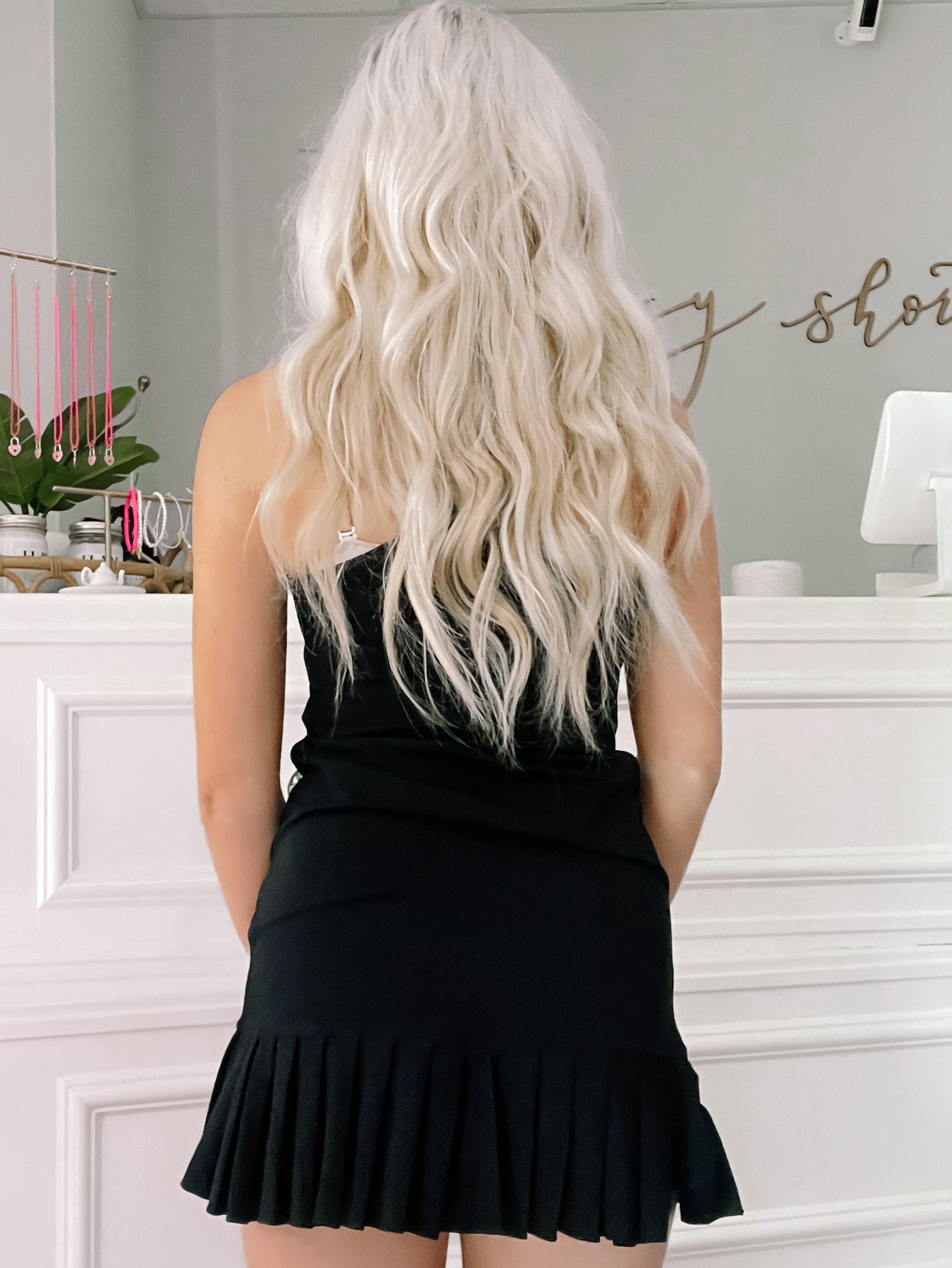 Black pleated mini dress shown from behind in a shop setting.