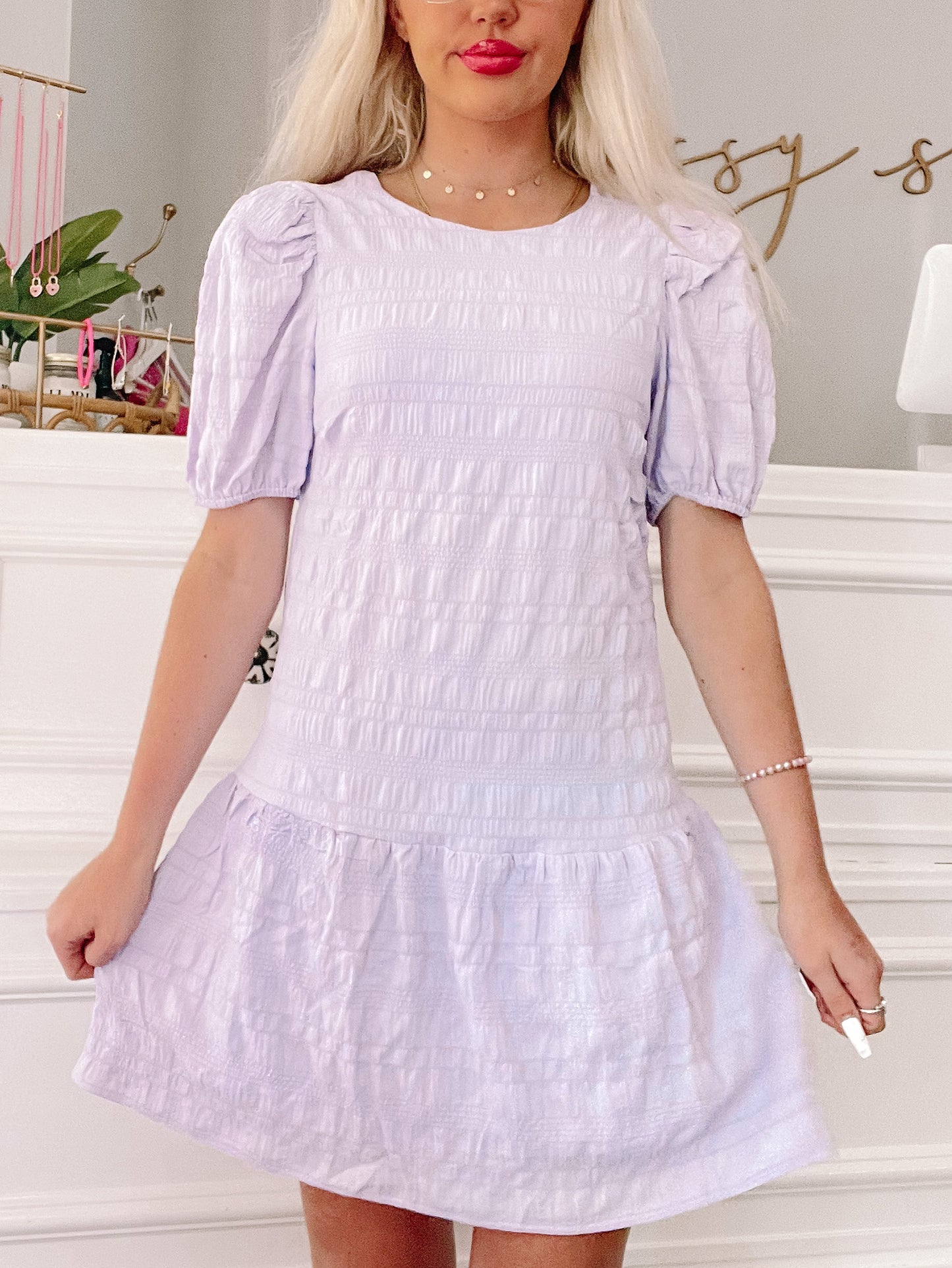 Lavender smocked mini dress with puff sleeves, shown on a model in a bright room.