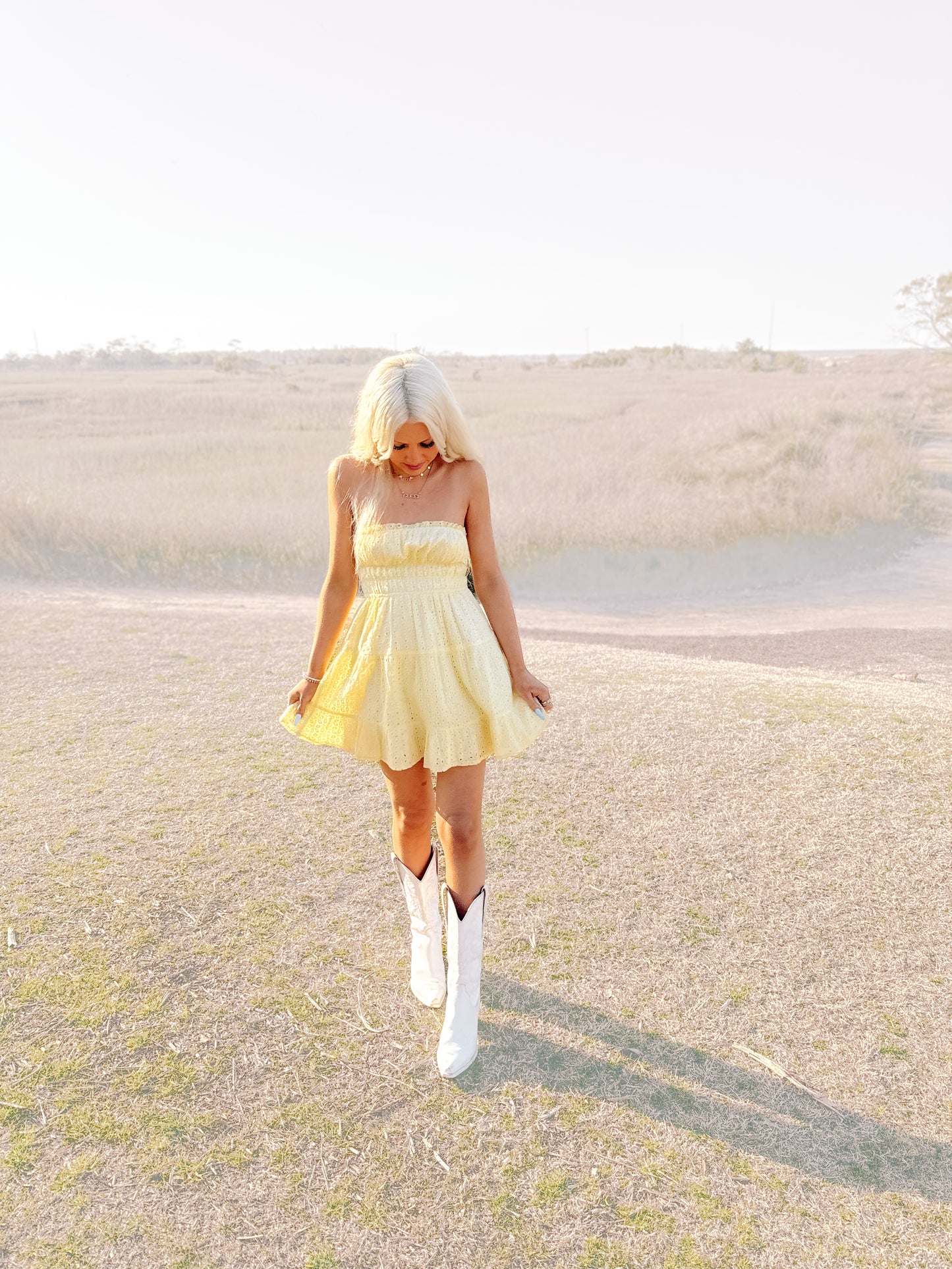 Pale yellow eyelet sundress styled outdoors, paired with white cowboy boots in a grassy field.