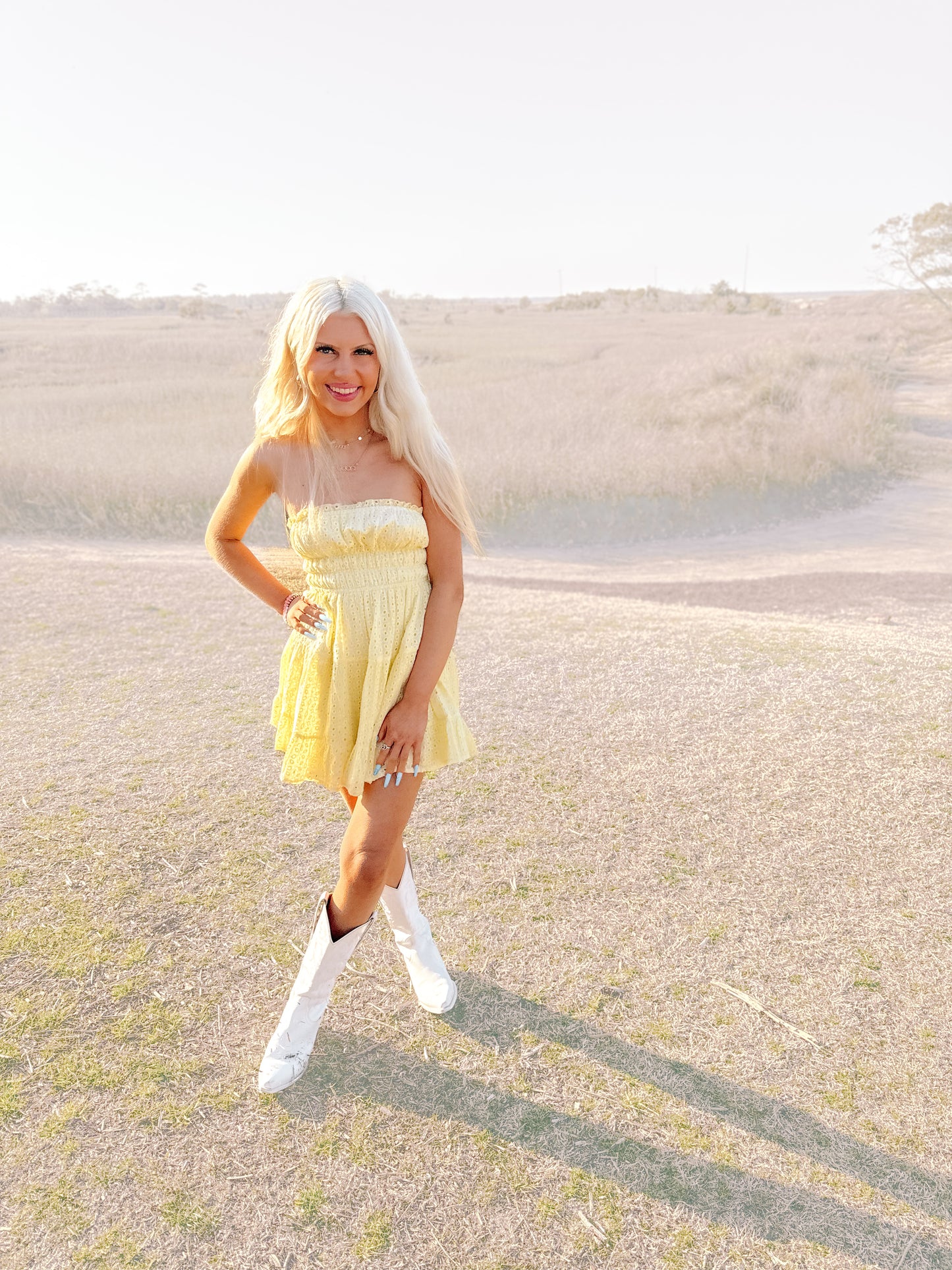 Yellow eyelet mini dress styled outdoors with white cowboy boots.