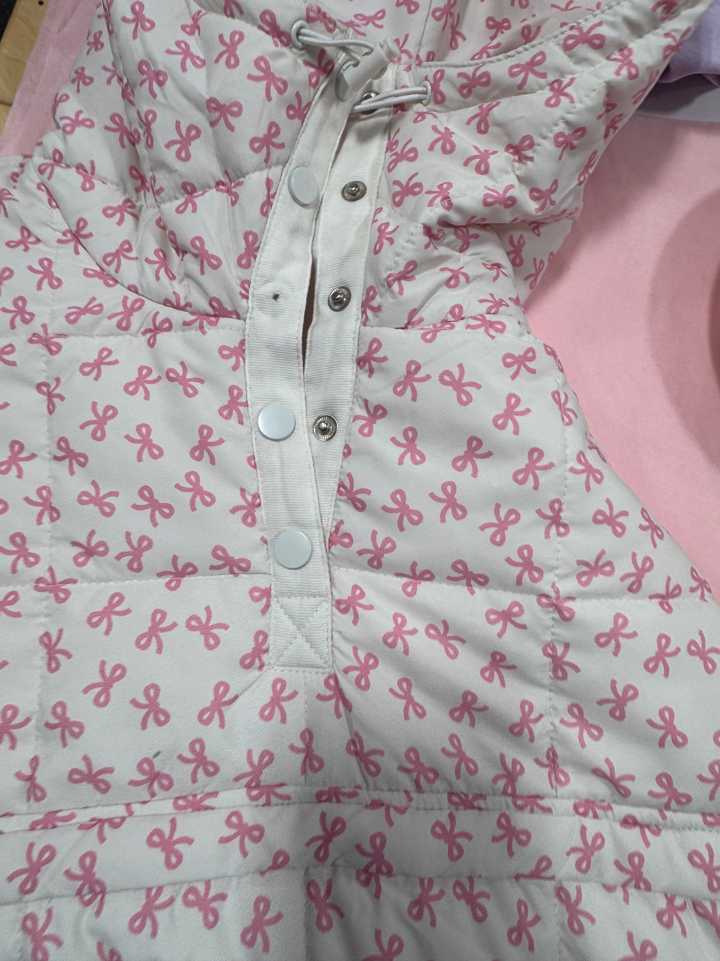 White quilted jacket featuring a pink bow pattern, shown buttoned.