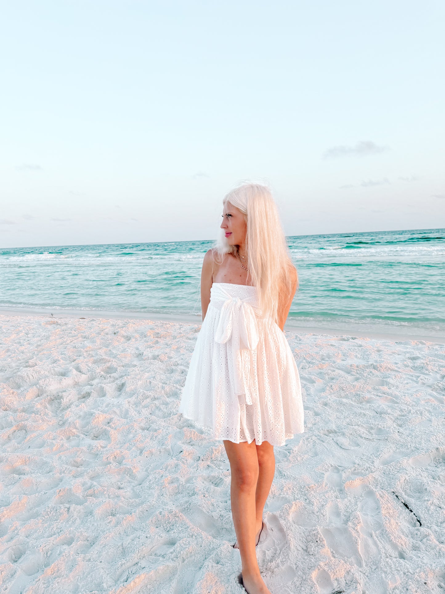 White eyelet mini dress on a beach at sunset.