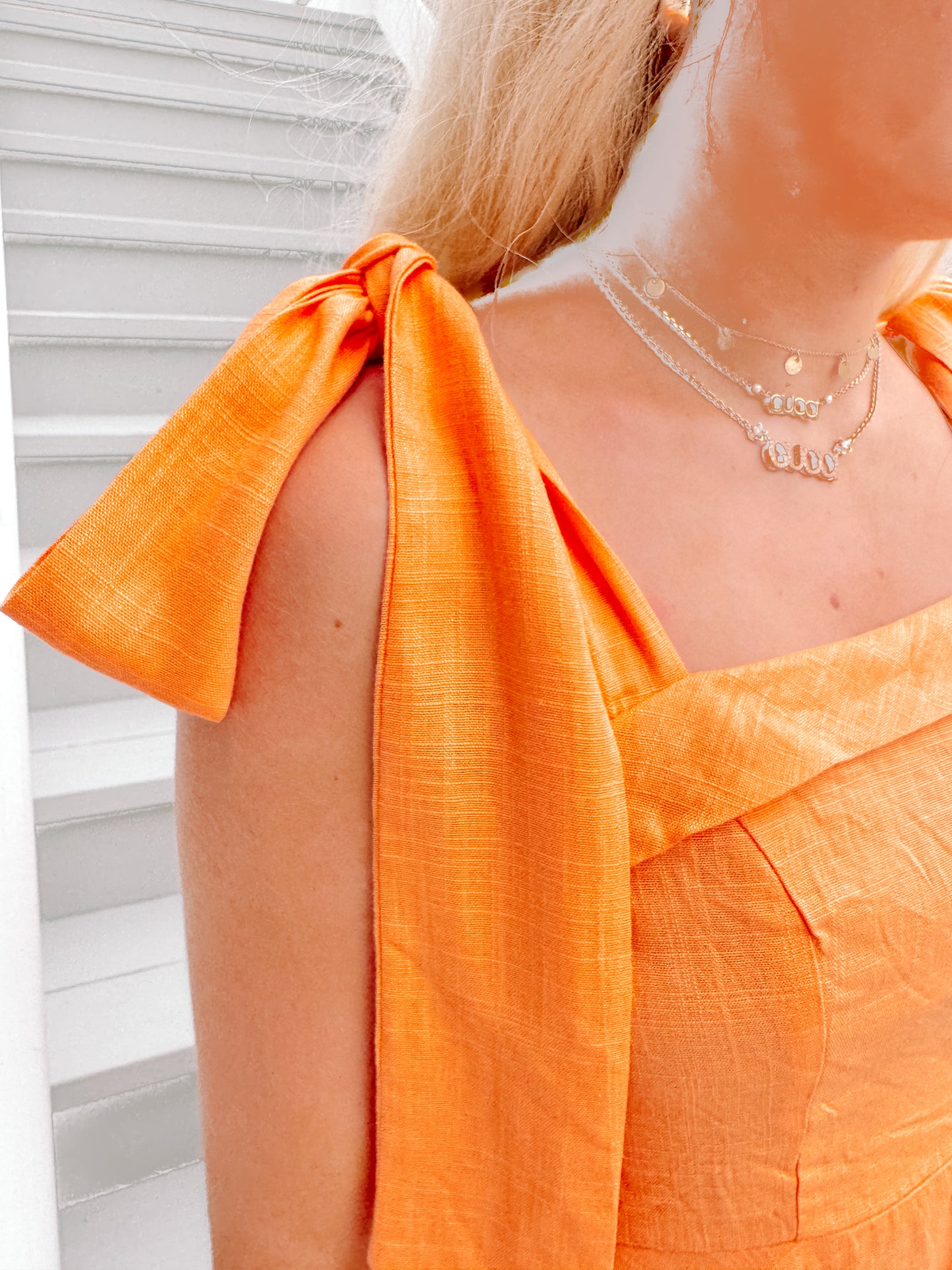 Close-up of bright orange summer dress with fabric tie shoulder straps, against a white background.