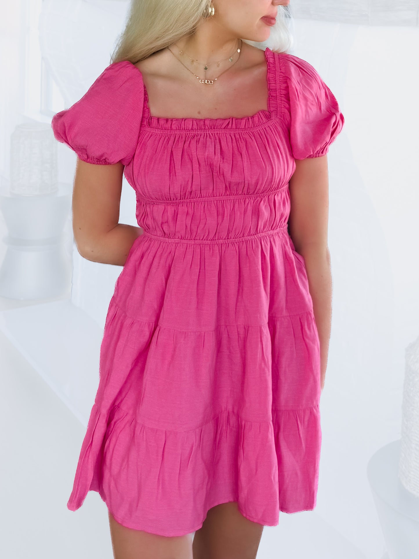 Hot pink tiered mini dress with puff sleeves, shown on a model against a white background.