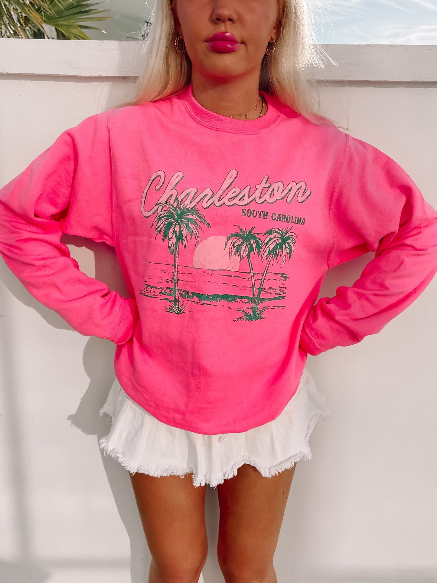 Hot pink crewneck sweatshirt with a palm tree graphic, styled with white shorts.